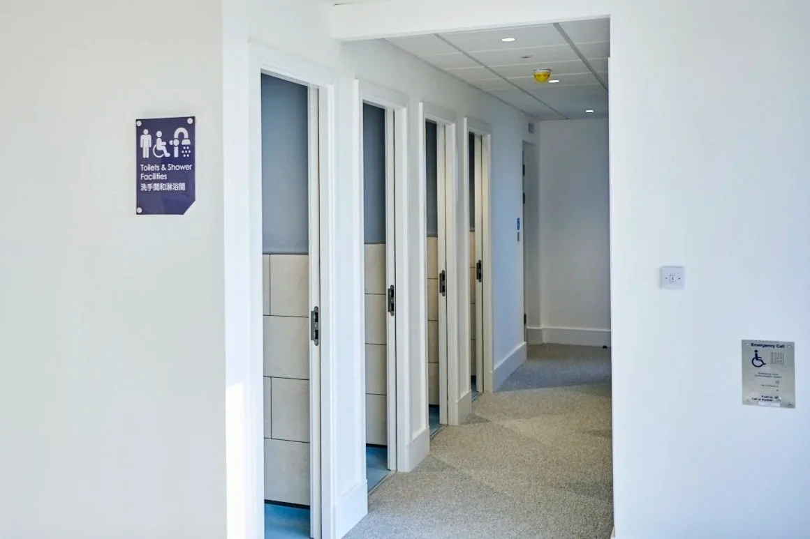 Hallway with four closed bathroom stalls and signs indicating toilets, showers, and handicap accessibility.