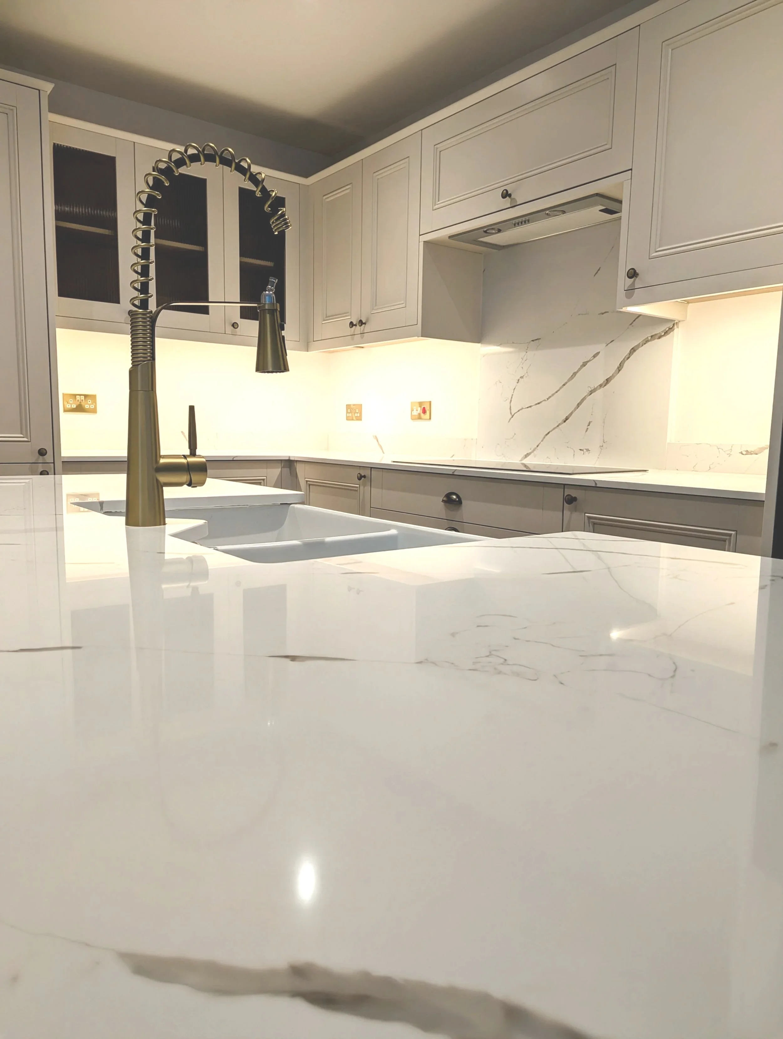 Modern kitchen with white marble countertops, a gold faucet, and white cabinetry.