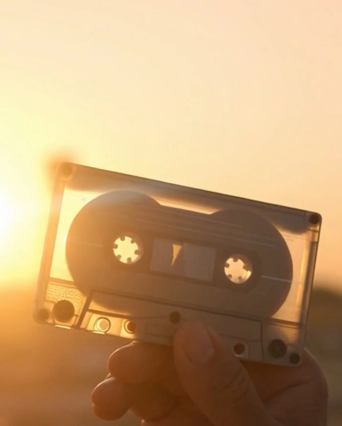 Close-up of a cassette tape held against a setting sun in the background.