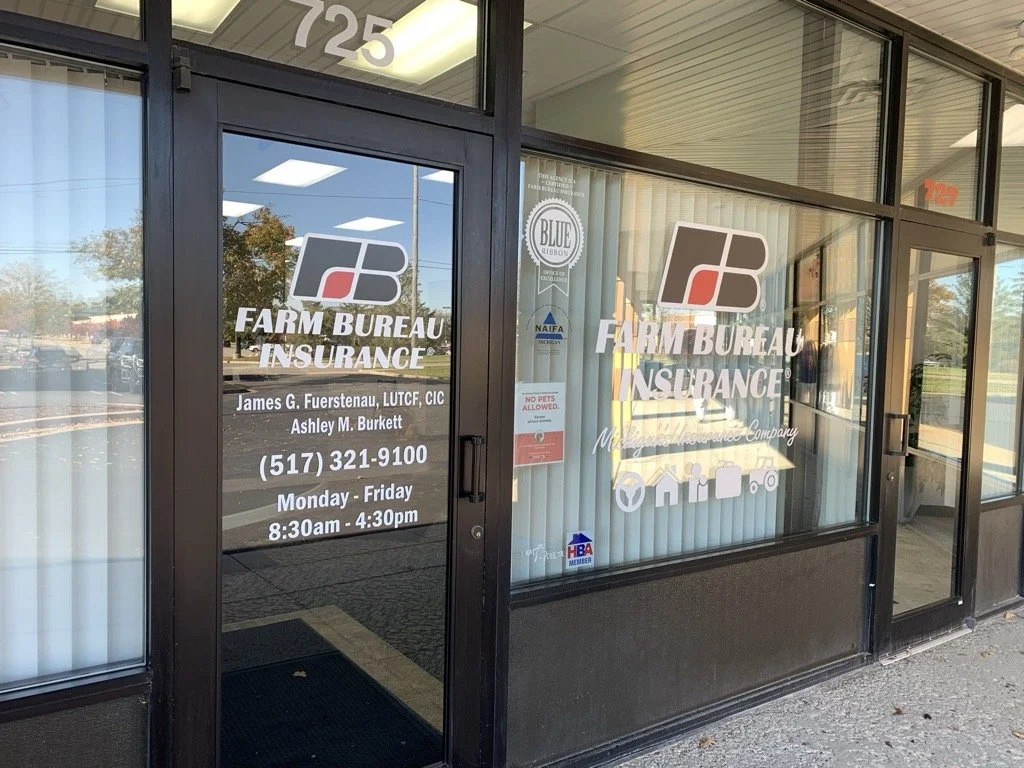 The storefront of a Farm Bureau Insurance office with glass doors and windows displaying the company logo, contact information, operating hours, and various service icons.