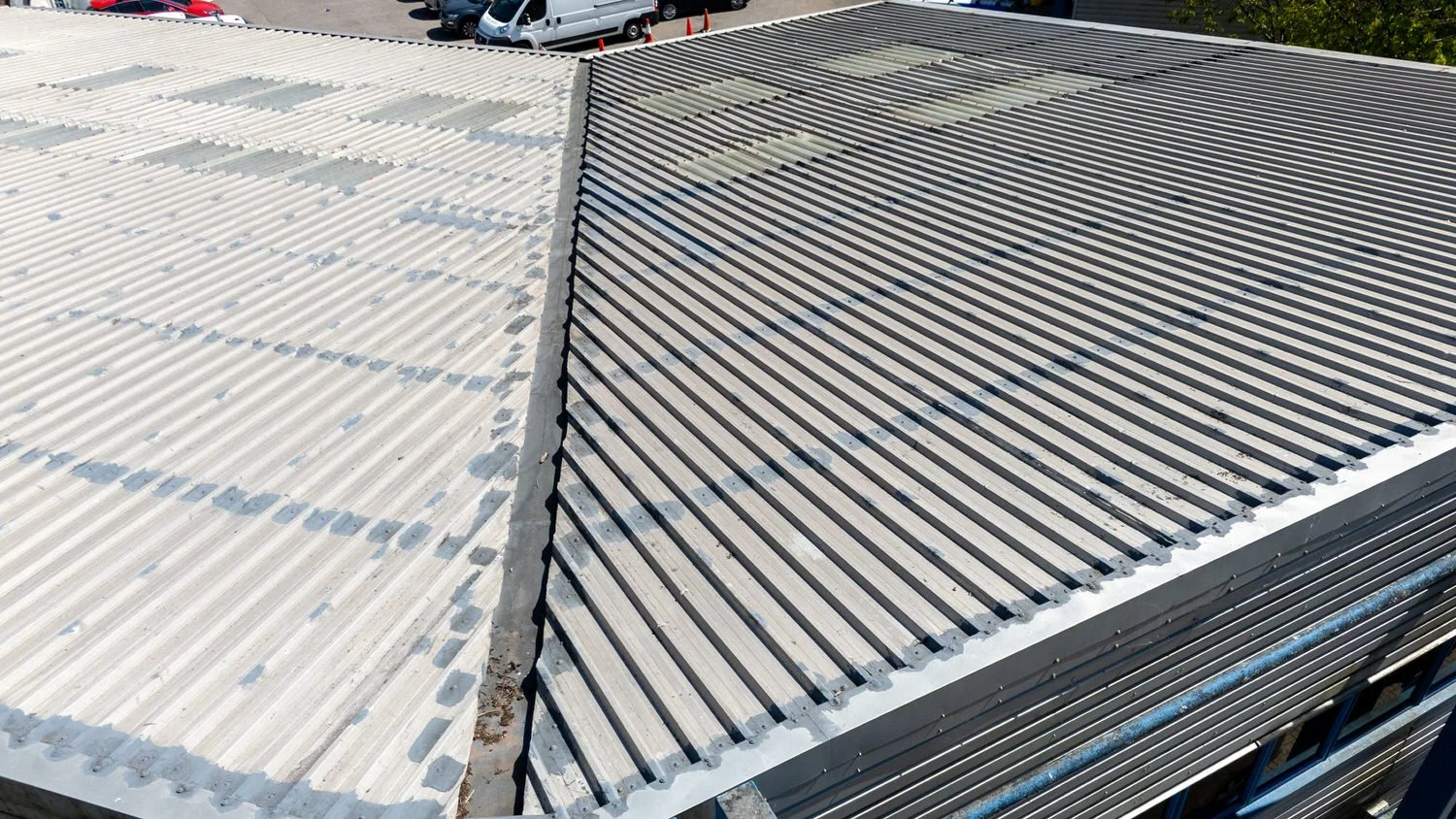 Aerial view of a corrugated metal roof in Swansea, half painted white, with vehicles in the background—perfect for a survey.