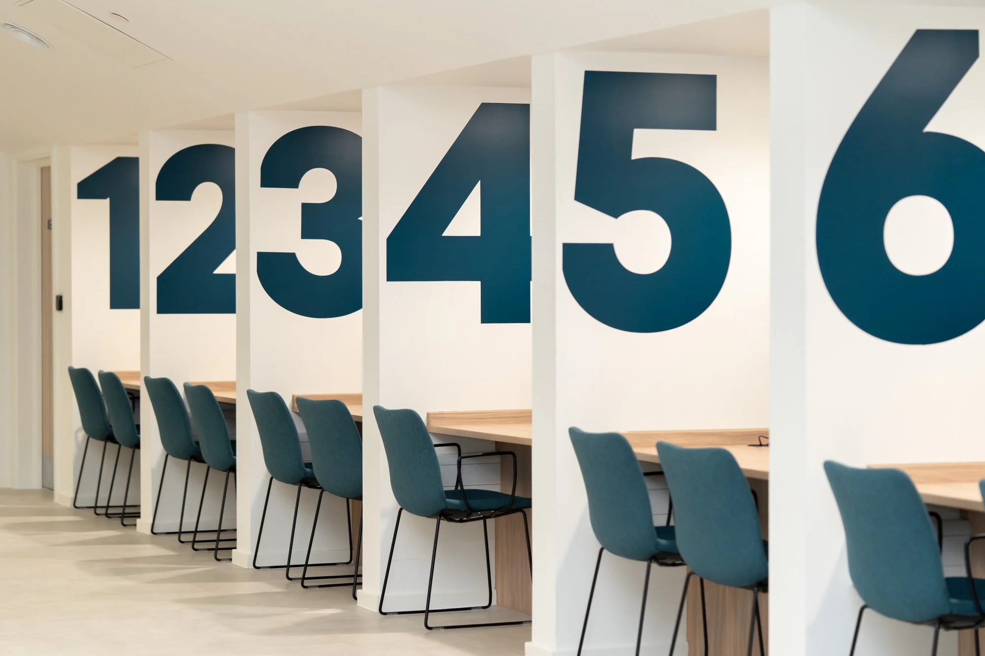 Bold large numbers 1 through to 6 above individual desks in alcoves at the Y Storfa hub in Swansea. Separate working booths with blue chairs.