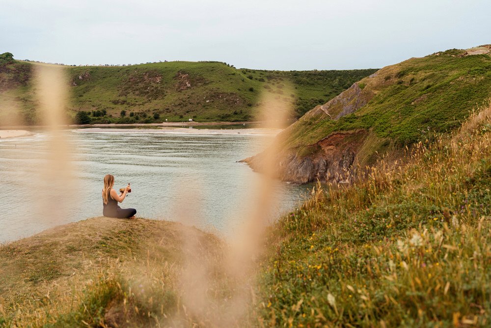 Yogi sat on a cliff looking over the sea of Three Cliffs Bay, holding a small gong bath