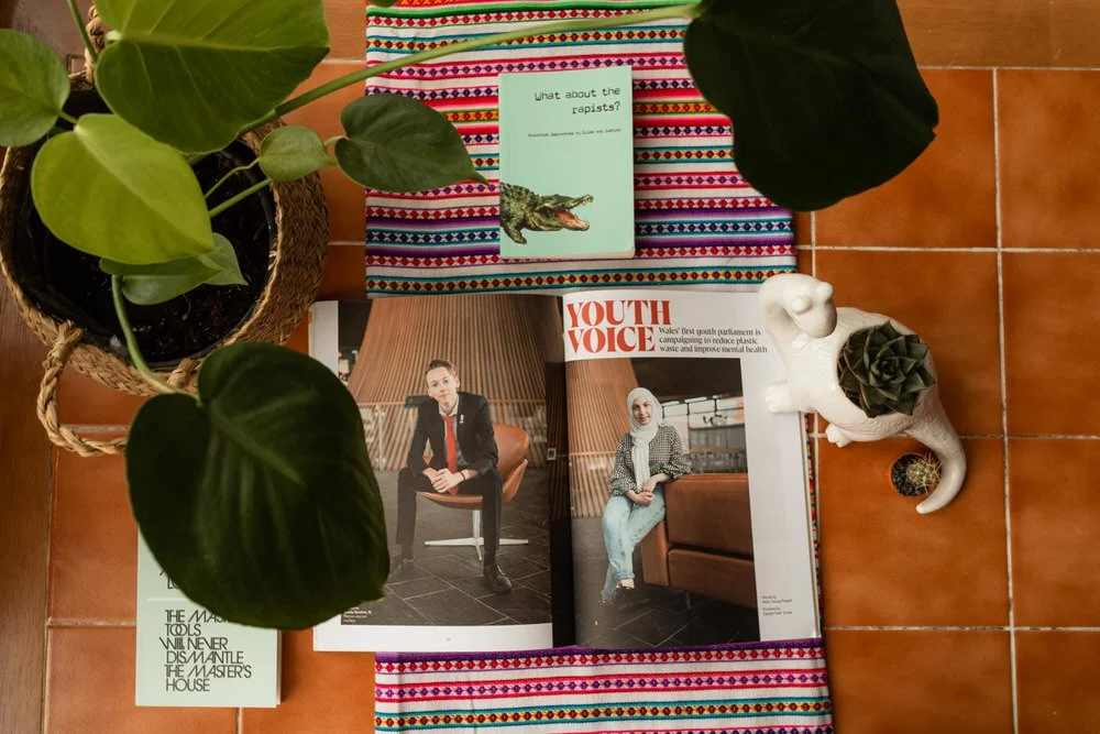 Magazine and book on a colorful tablecloth surrounded by potted plants and small decorative items.