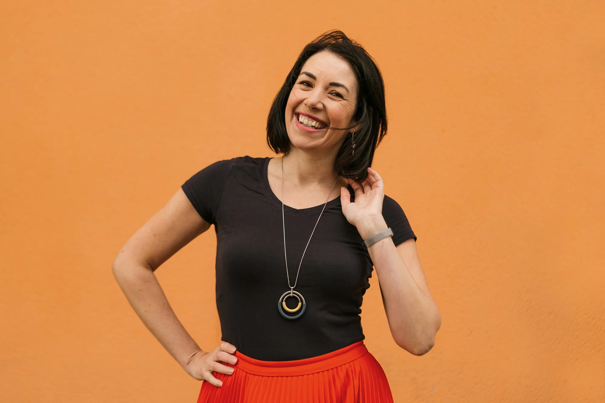 A happy smiling business woman having head shots done in a less boring way, set against an orange background.