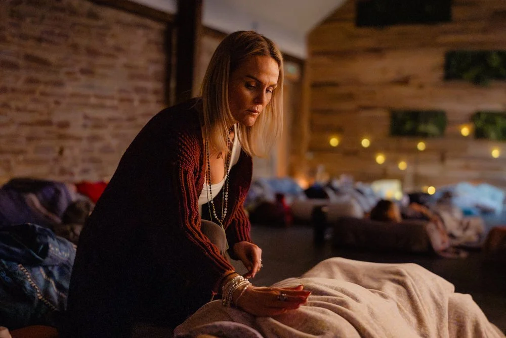 A reiki practitioner in a cozy room gently touches someone under a blanket, creating a calm, retreat-like therapeutic setting.