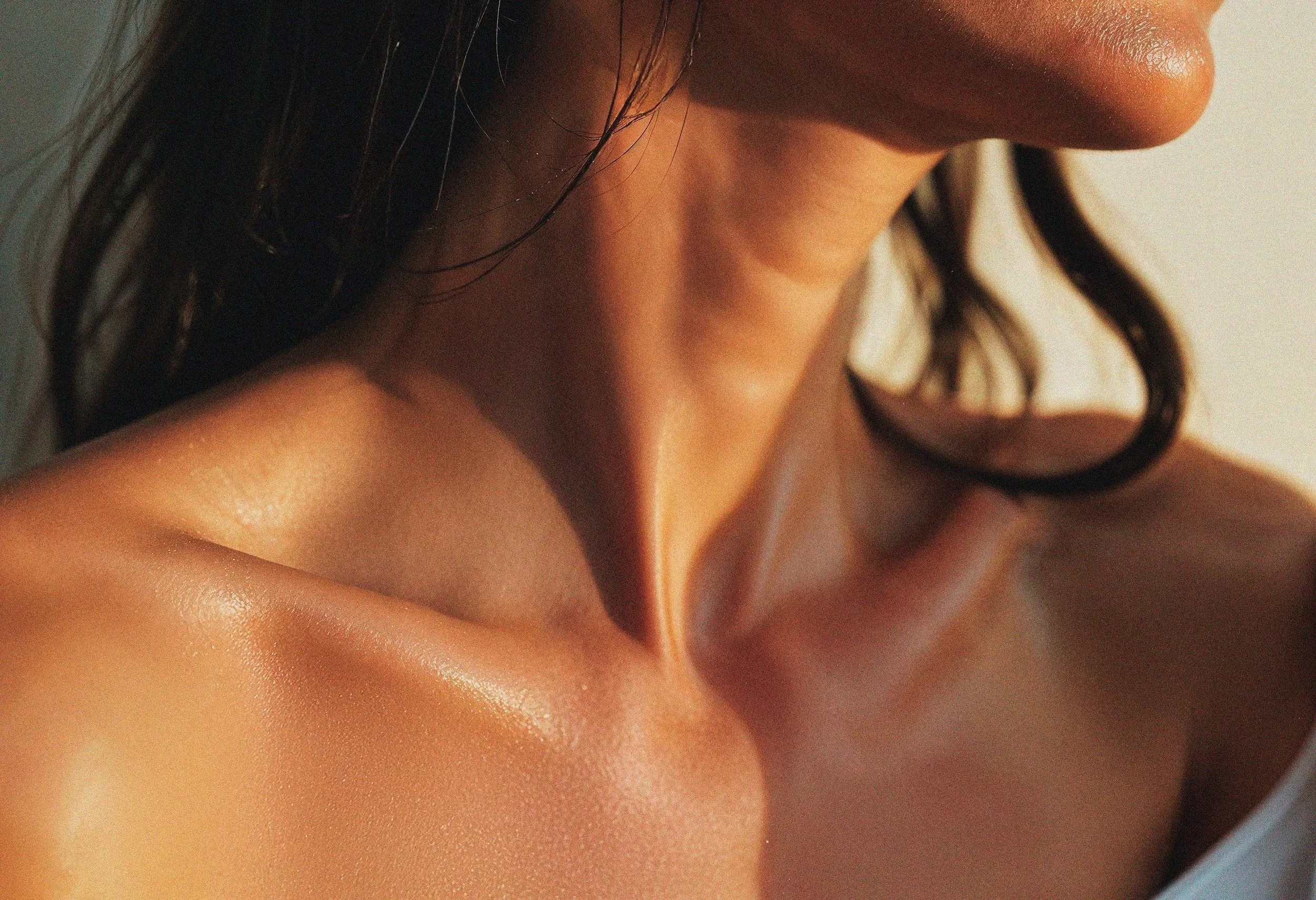 Close-up of a woman's shoulder, collarbone, and part of her chin, with sunlight highlighting her skin's texture.