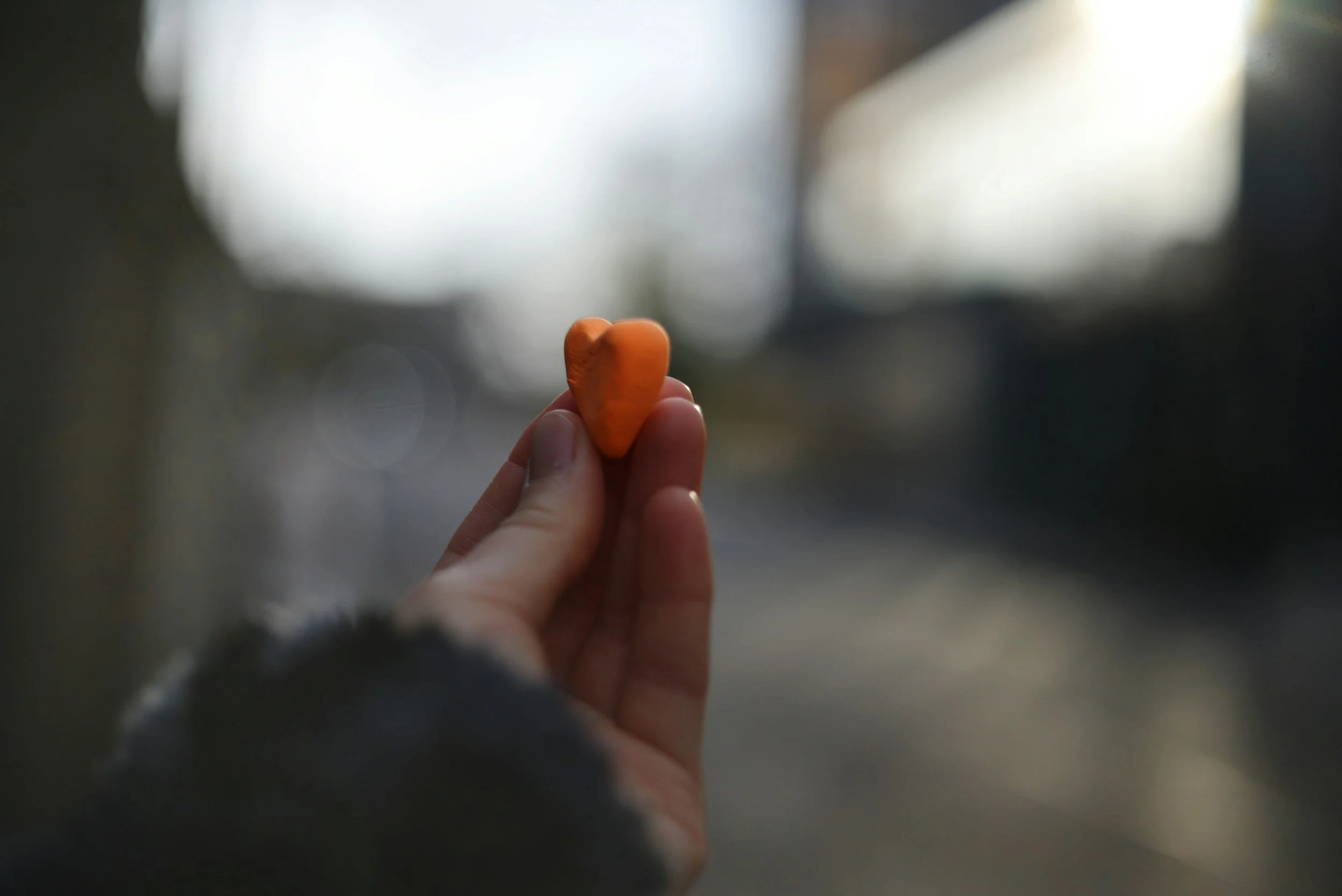A person holding a small orange heart-shaped object against a blurred background.