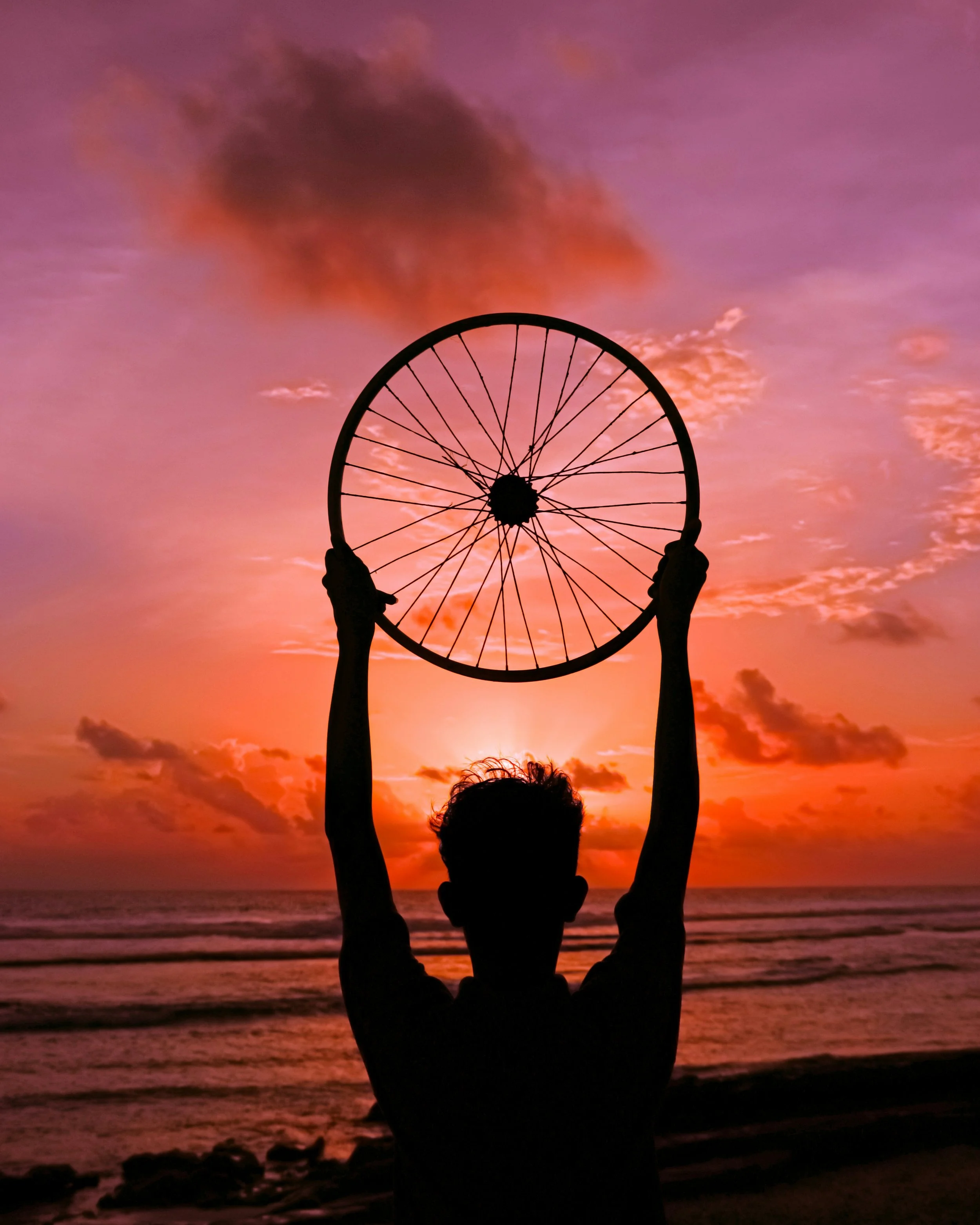 Silhouette of a person holding a wheels in front of a colorful sunset over the ocean.