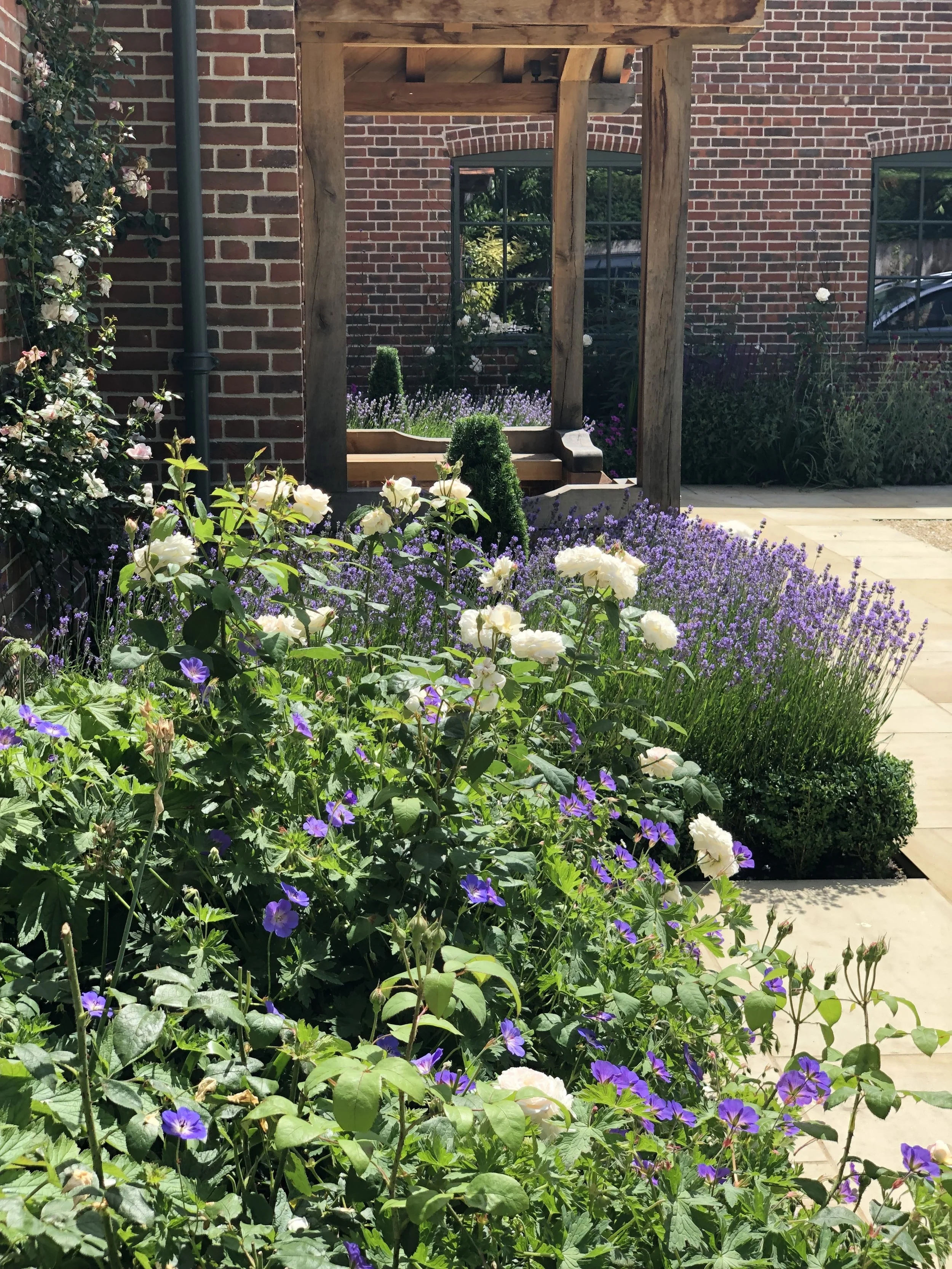 A garden with white and purple flowers in front of a brick building with a wooden gazebo.