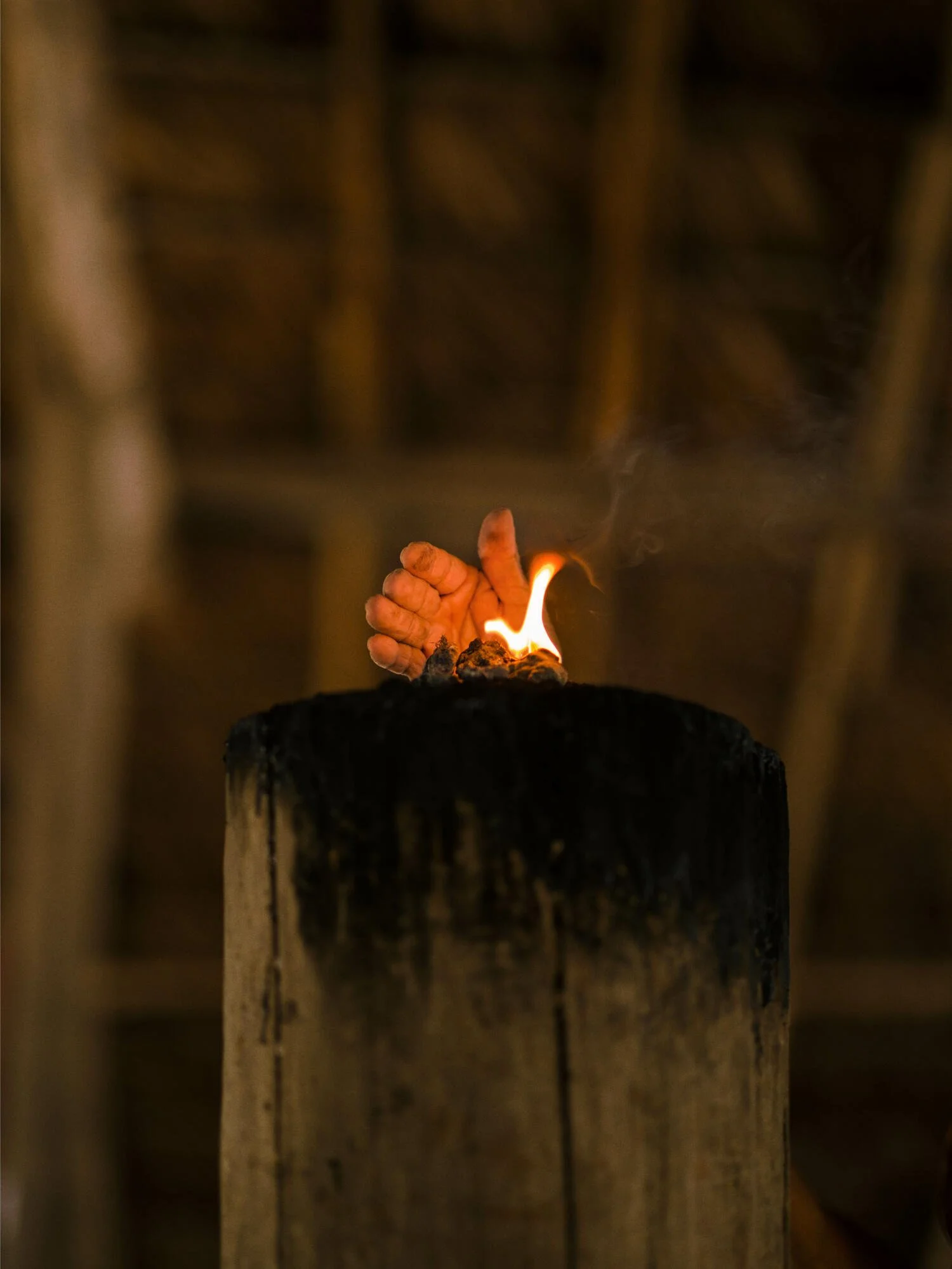 A small flame burning on a piece of wood, with some smoke rising from it.