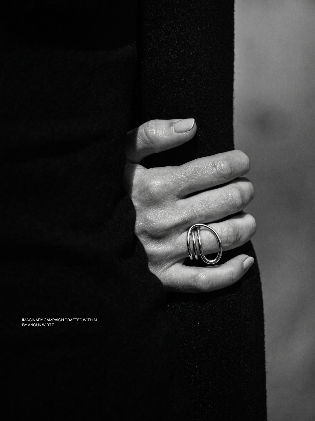Close-up of a person's hand wearing a ring, resting on a dark fabric background.
