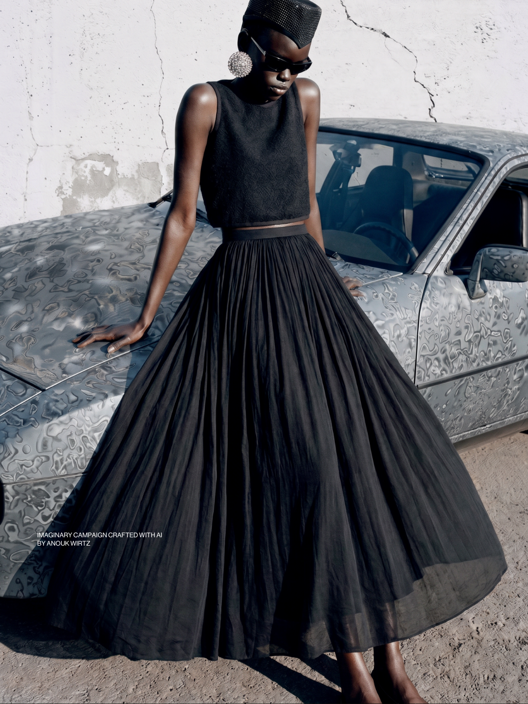 A woman dressed in black fashion standing next to a stylized silver car against a white wall.