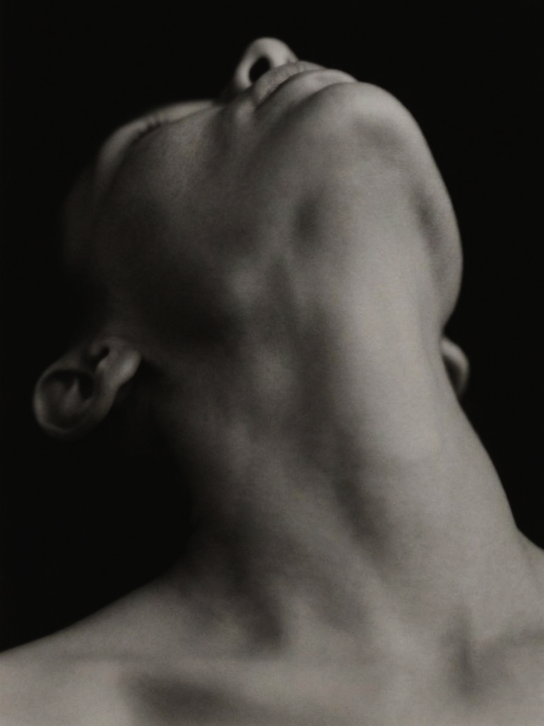Close-up black and white photograph of a person's face tilted back with eyes closed, emphasizing facial features and neck.