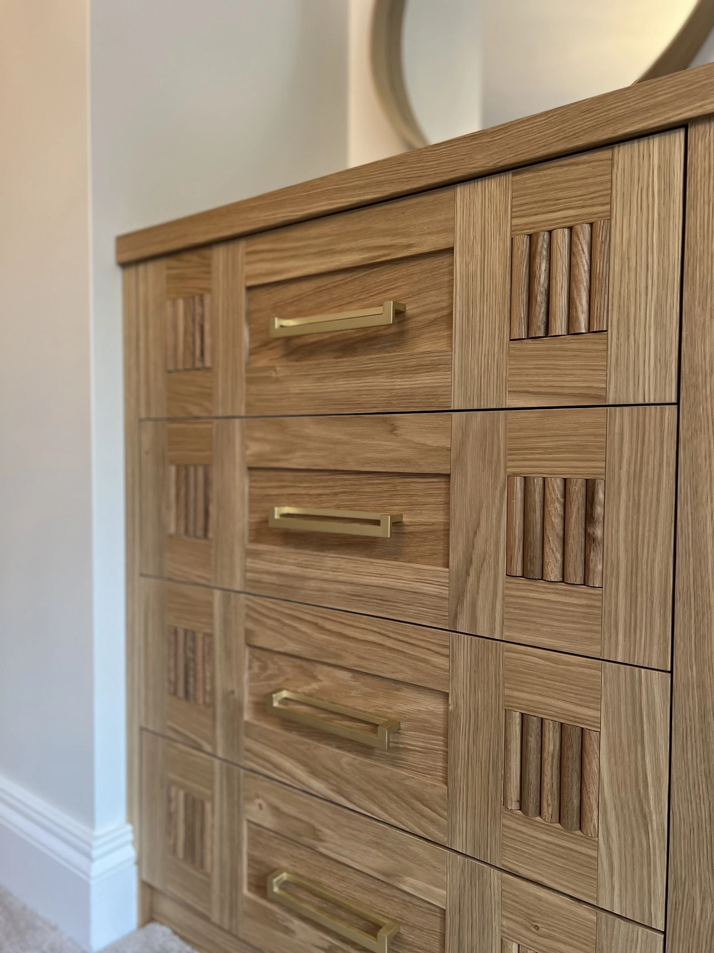 Close-up image of a wooden dresser with brass handles and a decorative pattern of vertical wood slats on the drawer panels.