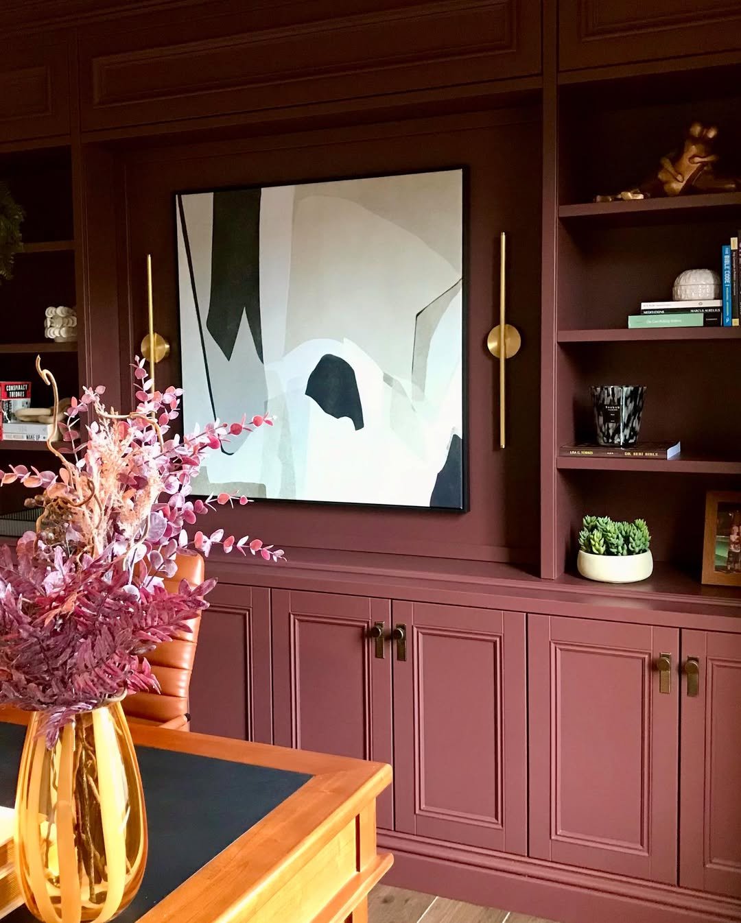 Interior of a room with built-in cabinetry, a large abstract panda art piece on the wall, a floral arrangement on a wooden table, and books on the shelves.