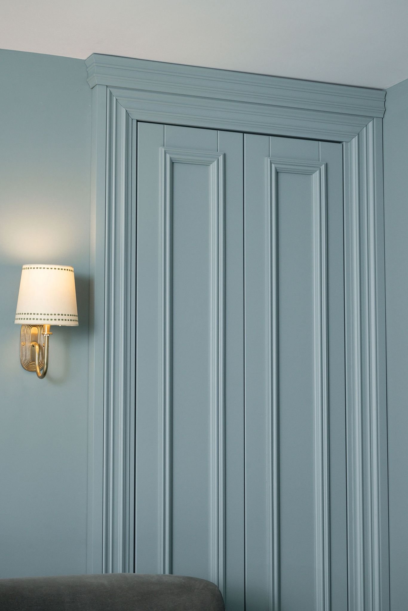 Blue closet doors with detailed molding and a wall-mounted lamp with a white shade.