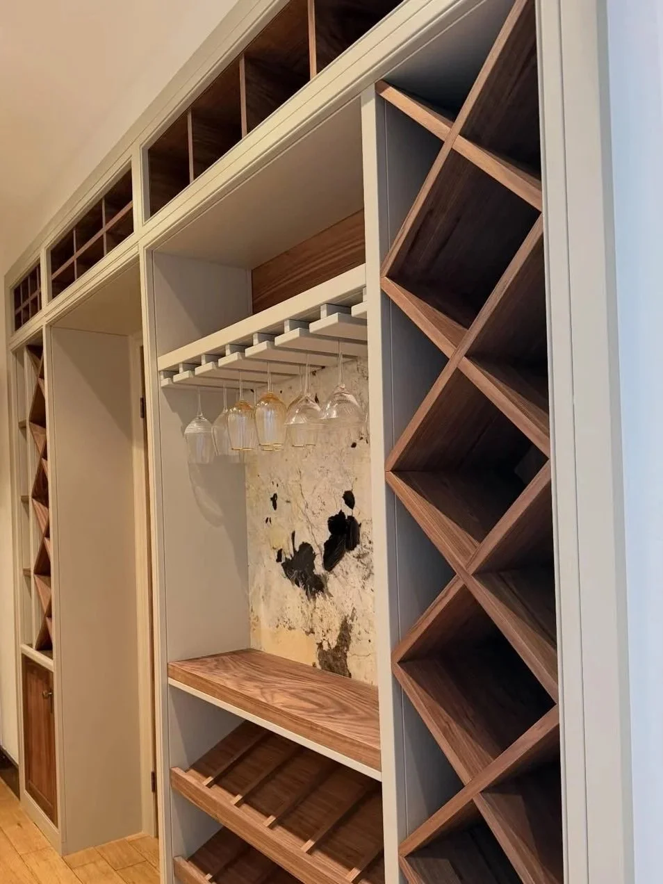Built-in wine storage with wine glass holder and a textured wall behind it, featuring dark and light wood cabinetry and diagonal wine racks.