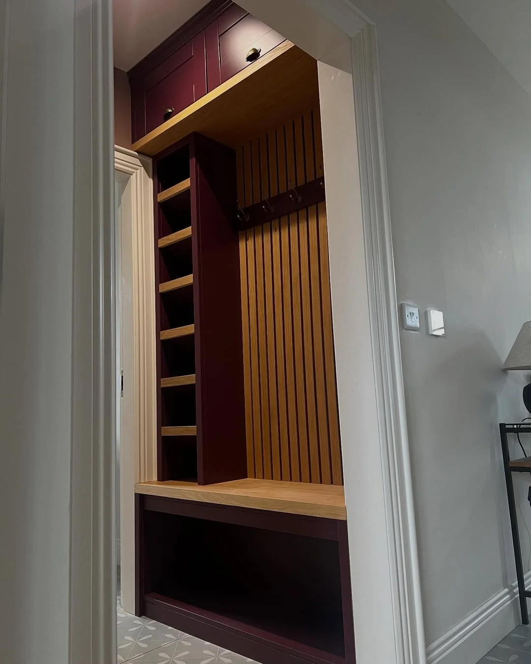 Interior view of a built-in closet with shelves, hooks, and wood paneling, located in a room with beige walls and patterned flooring.