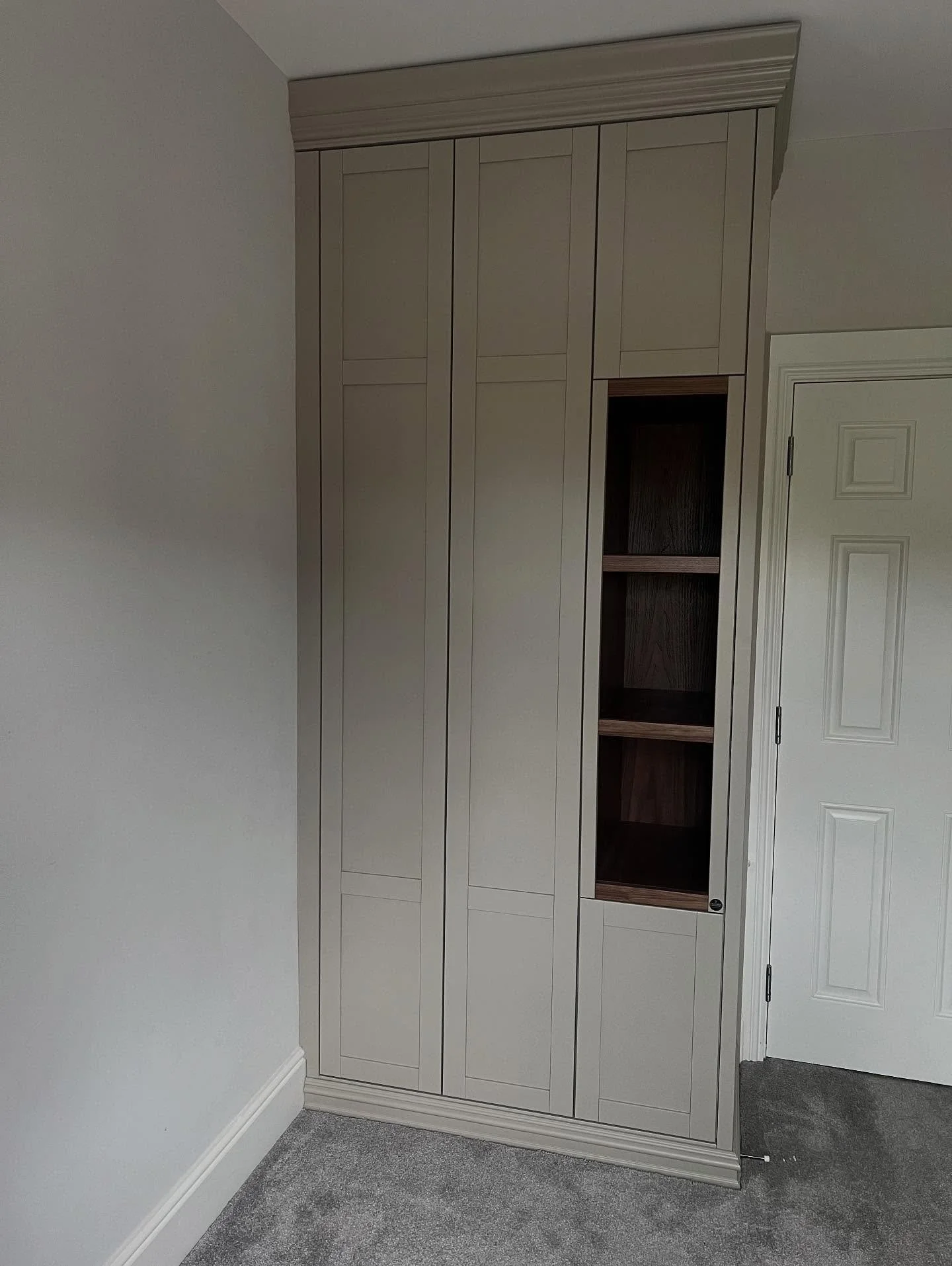 Built-in beige cabinet with open shelves near a white door in a room with gray carpet.