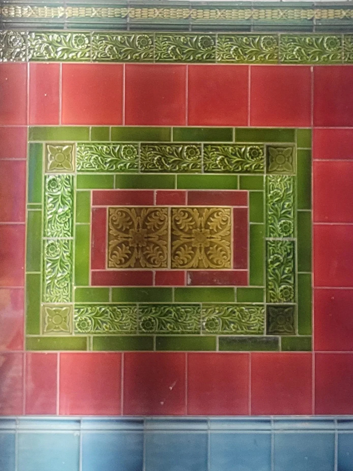 Close-up image of patterned ceramic tiles in red, green, yellow and black, arranged in a decorative rectangular design.