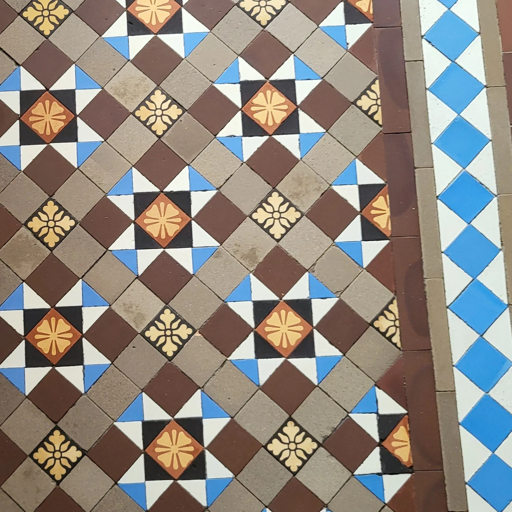 Patterned tile floor with geometric designs in brown, white, blue, black, and orange colors.