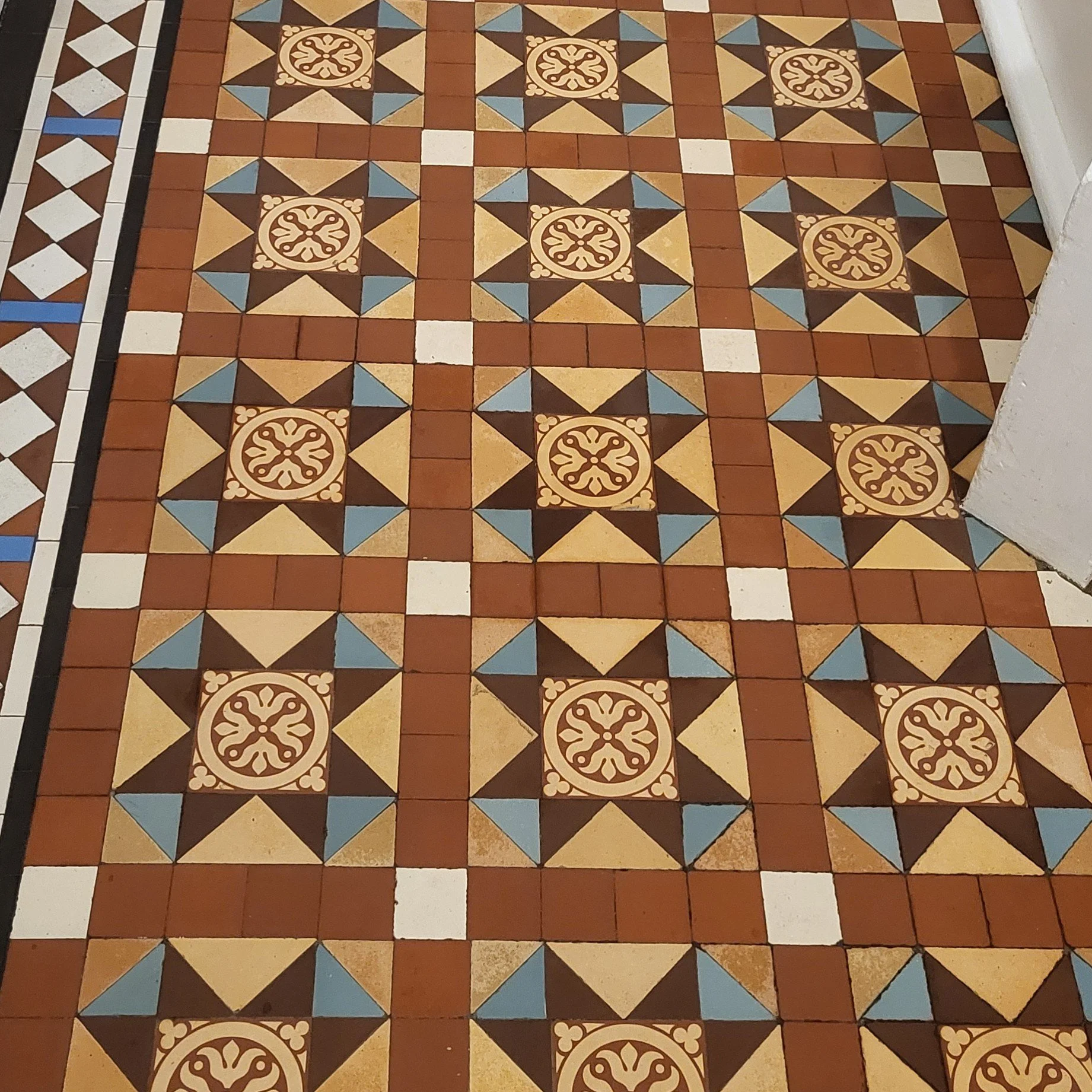 Typical busy Victorian tiled floor scheme with small tiles tesselating to form a larger square which is framed with red tiles and motifs repeated across the floor