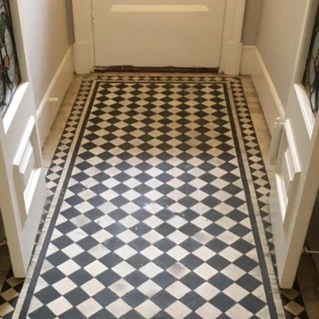 A black and white checkered tile floor in a narrow entryway, with white doors on either side and a white door at the end.