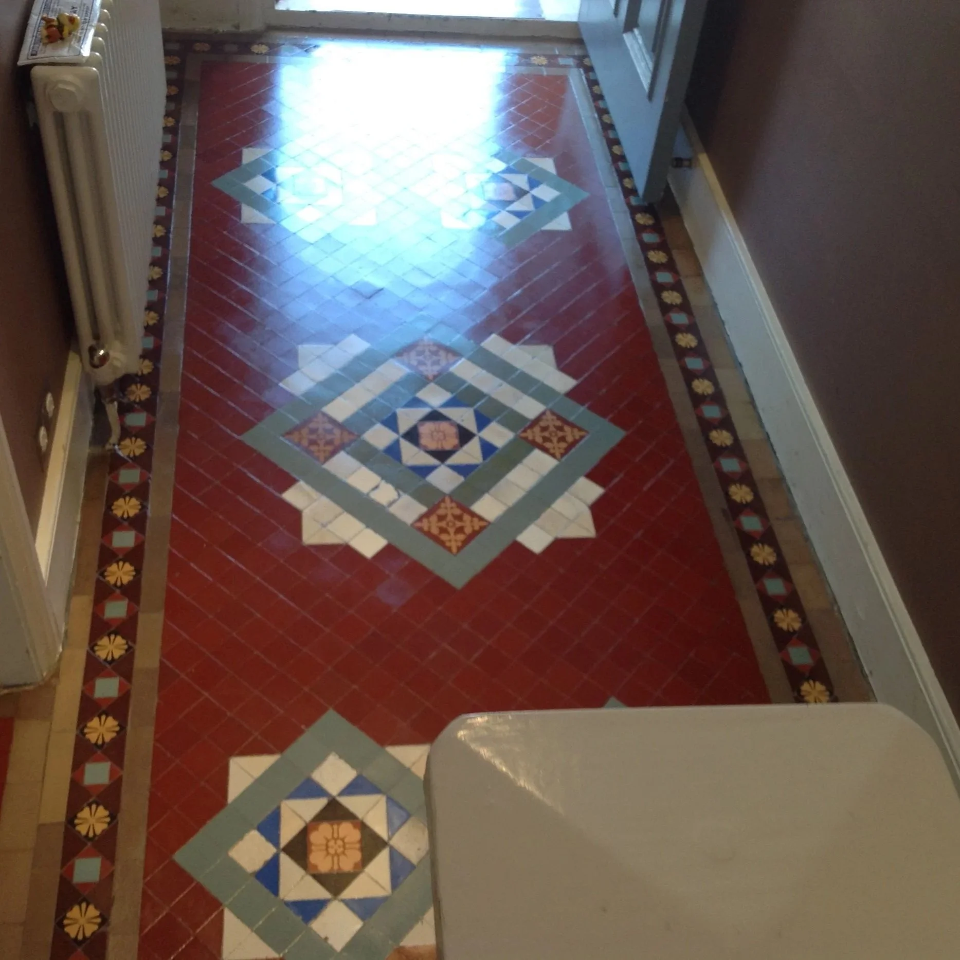 Decorative tile floor with geometric patterns in blue, white, red, and beige, bordered by a floral design with yellow flowers and red diamonds.