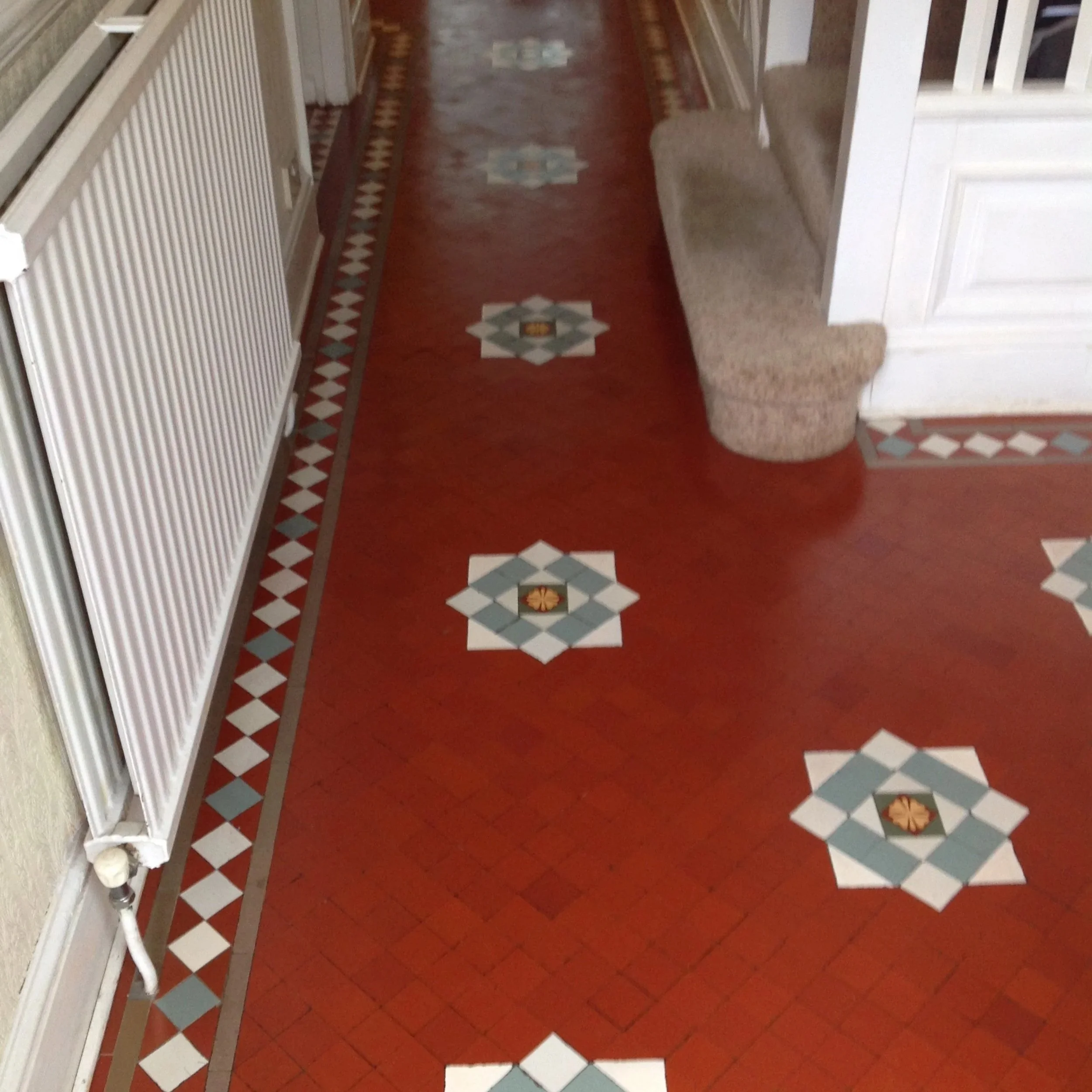 Red tile floor with decorative patterns and a staircase with carpeted steps leading upstairs.