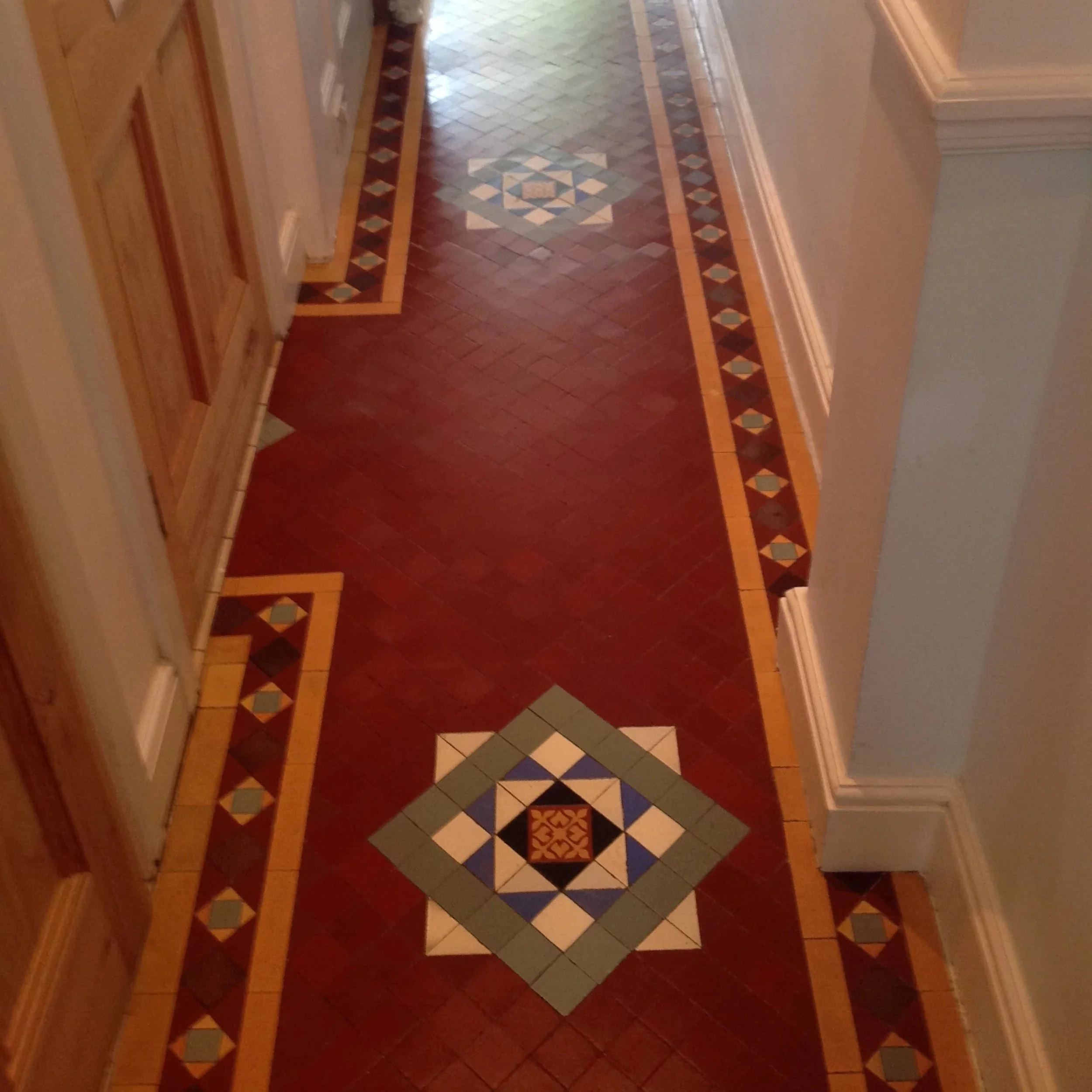 Decorative tiled pattern on a wooden floor in a hallway.