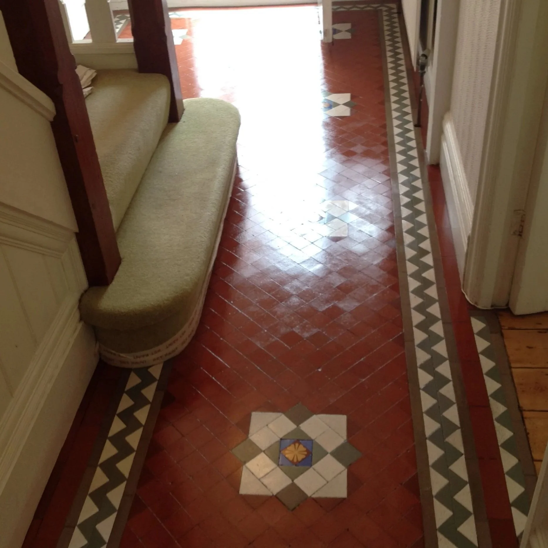 Indoor hallway with a decorative tiled floor and a green cushioned bench.