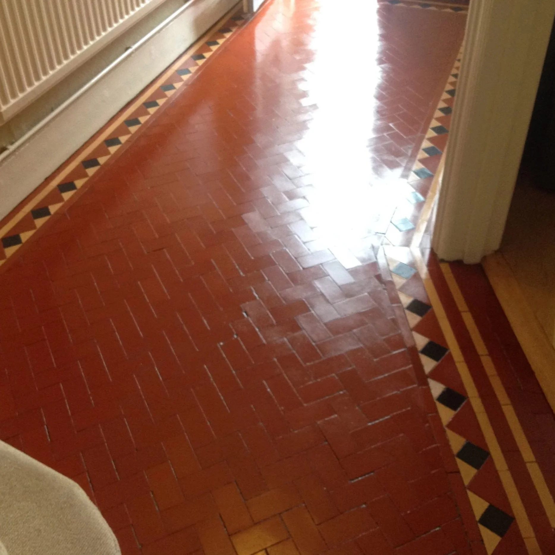 Red herringbone tile floor with a decorative border along the edge, near a doorway and radiator.