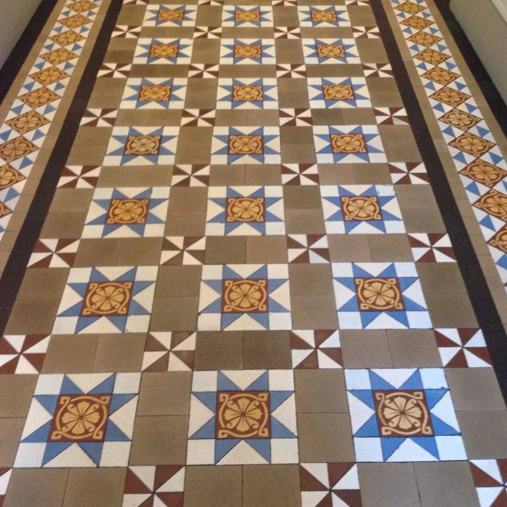Decorative tiled floor with a pattern of brown, white, blue, and orange tiles, featuring a central floral design.