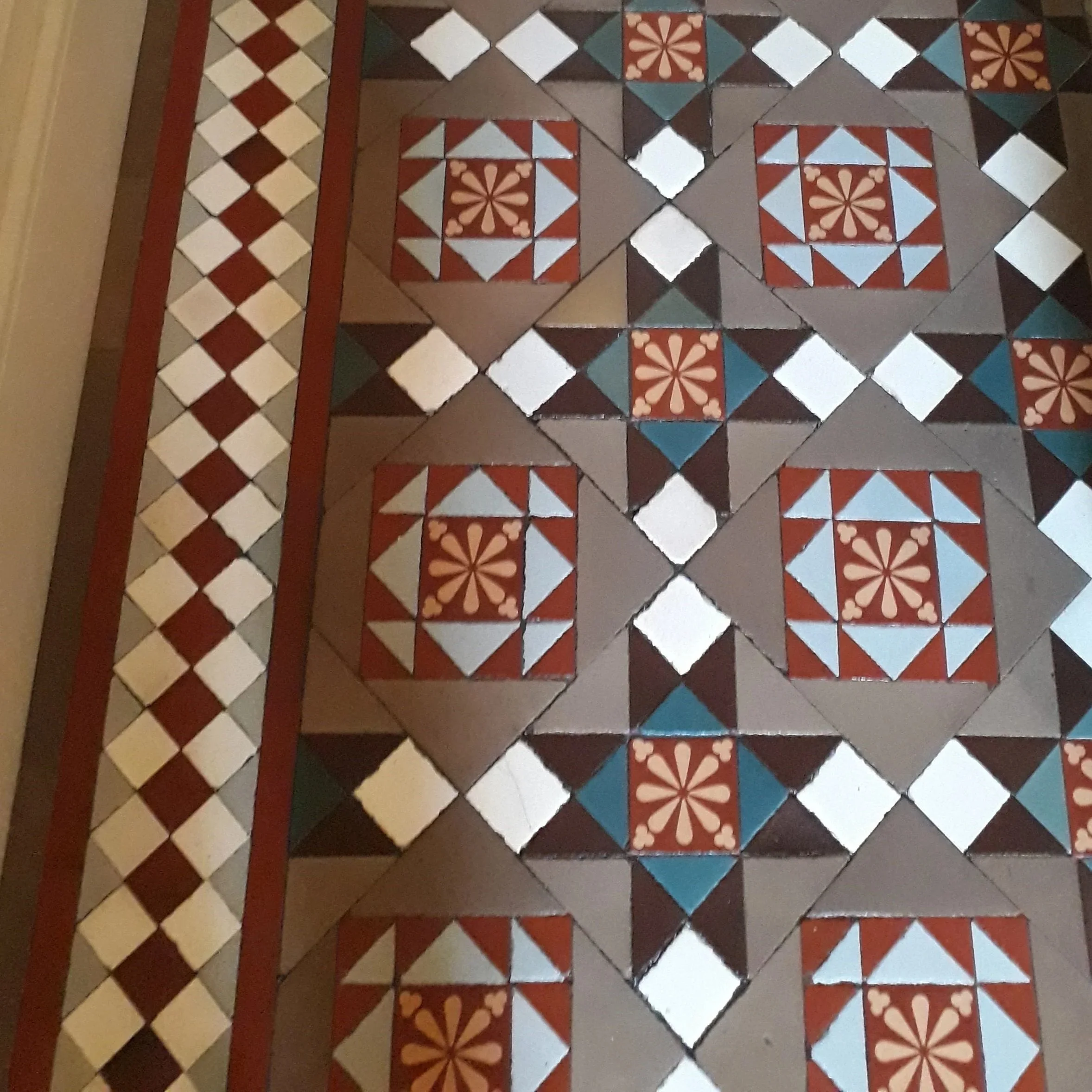 Close-up of decorative vintage tile floor with geometric and floral patterns in red, brown, blue, black, and white colors.