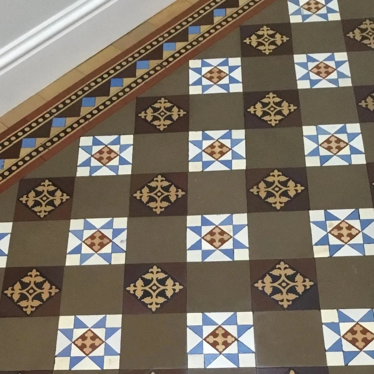 Close-up of a patterned tile floor with a geometric design in blue, white, brown, and black, alongside a border with smaller blue and black tiles.