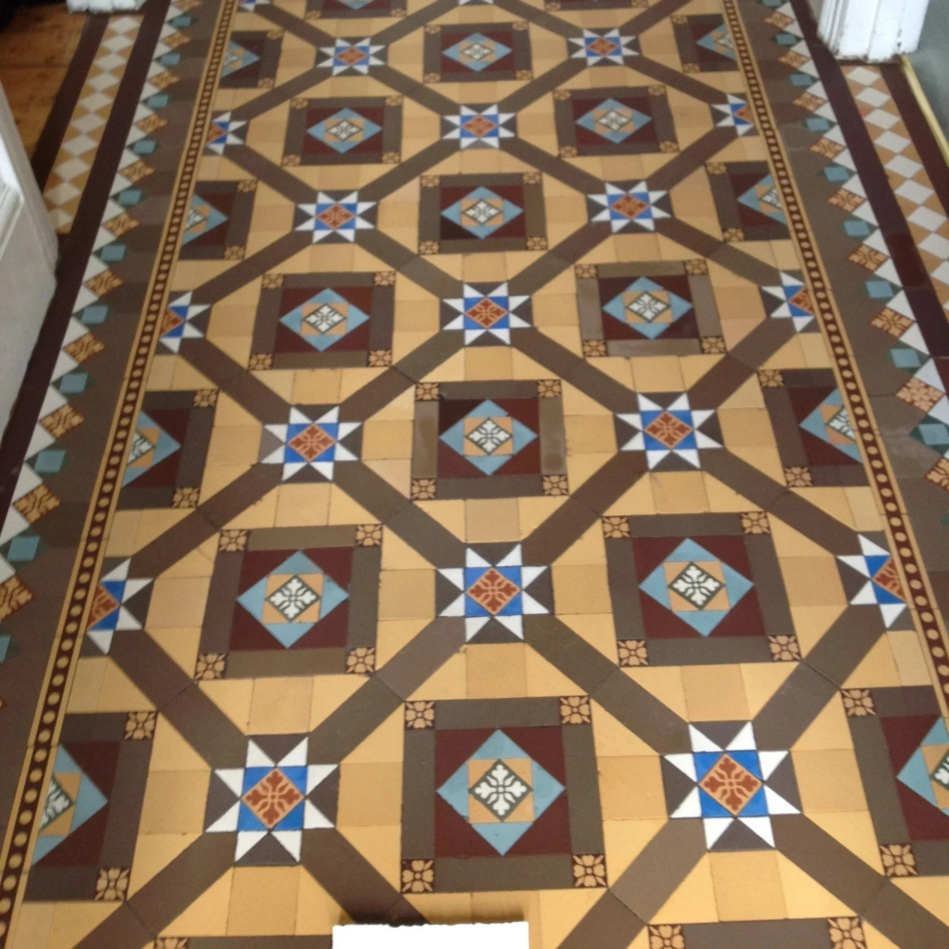 Decorative patterned tiled floor with geometric shapes and colors, including beige, brown, white, blue, and red, forming a repeating symmetrical design.