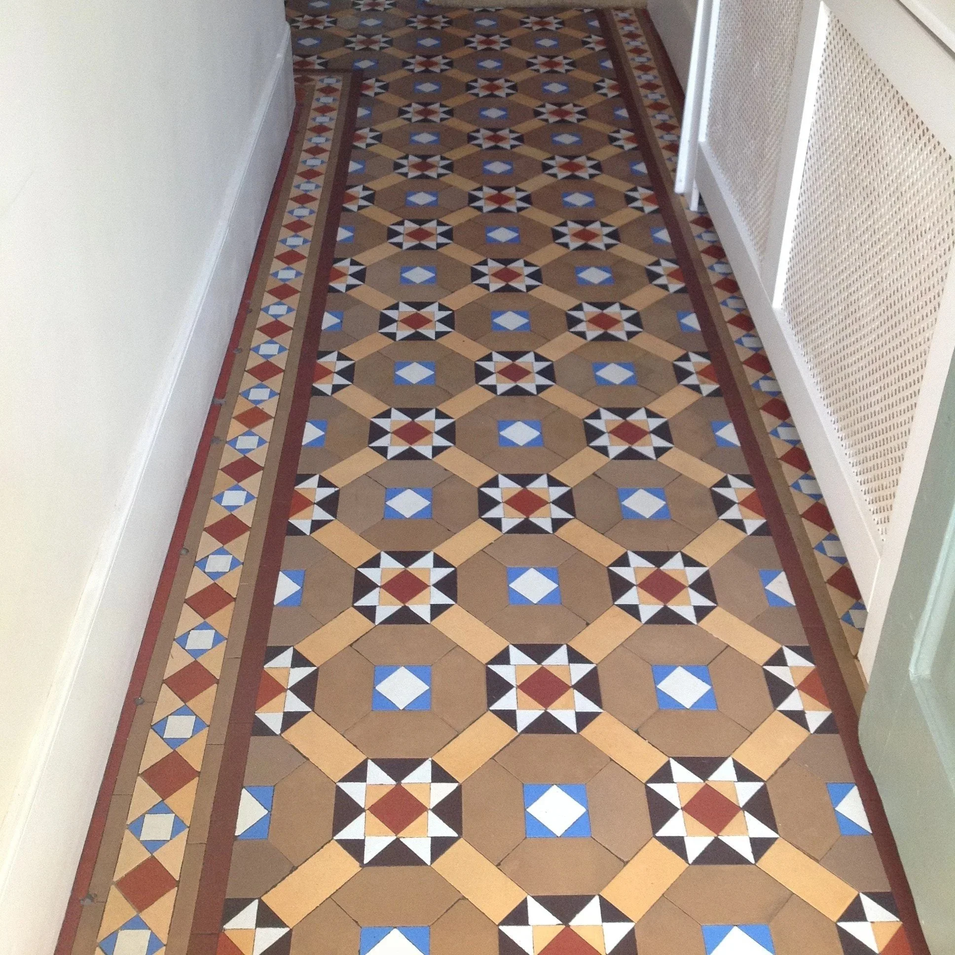 Decorative patterned tile floor in an interior hallway with a white wall on the left and a radiator cover on the right.