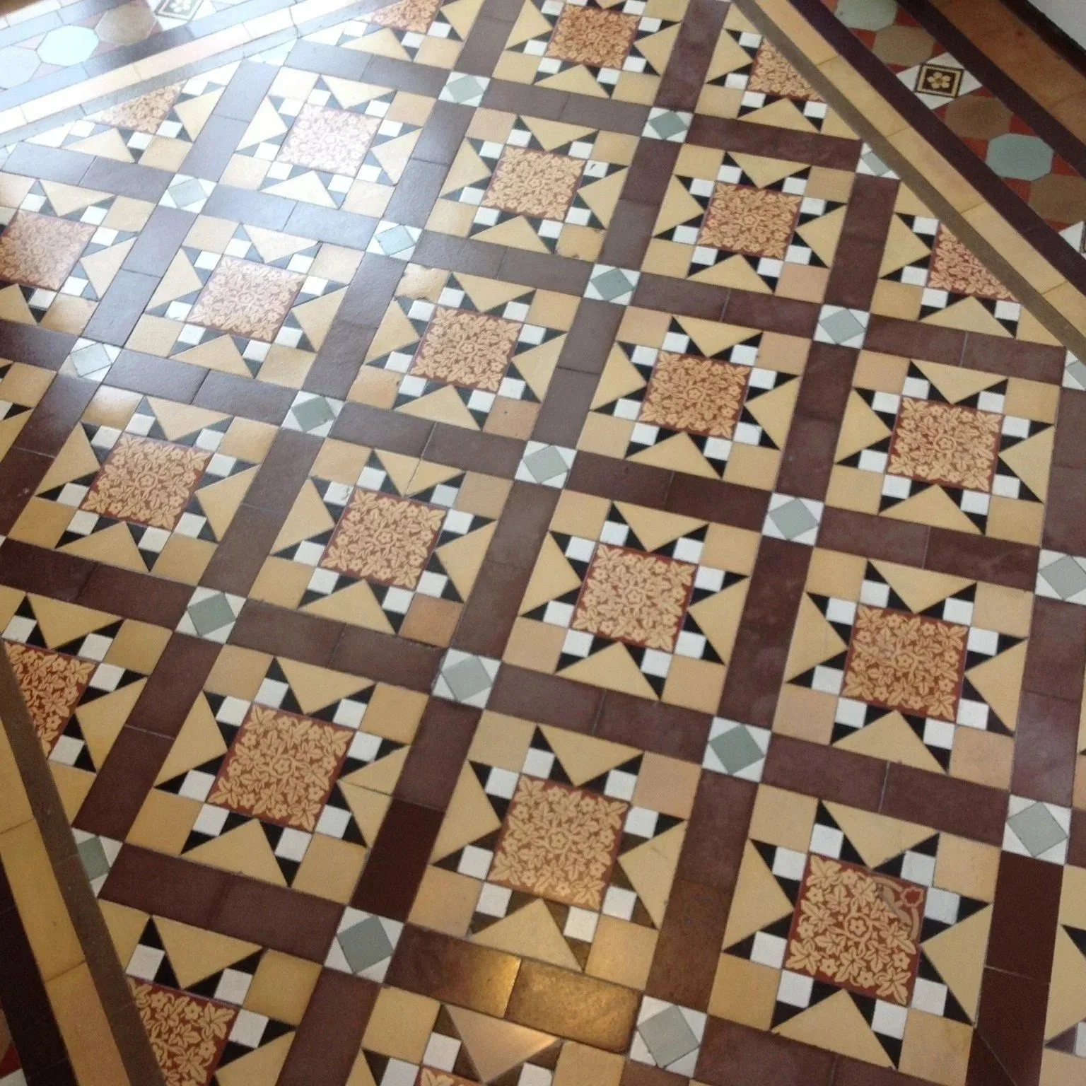 Patterned tile floor with geometric and floral designs in brown, cream, black, green, and beige colors.
