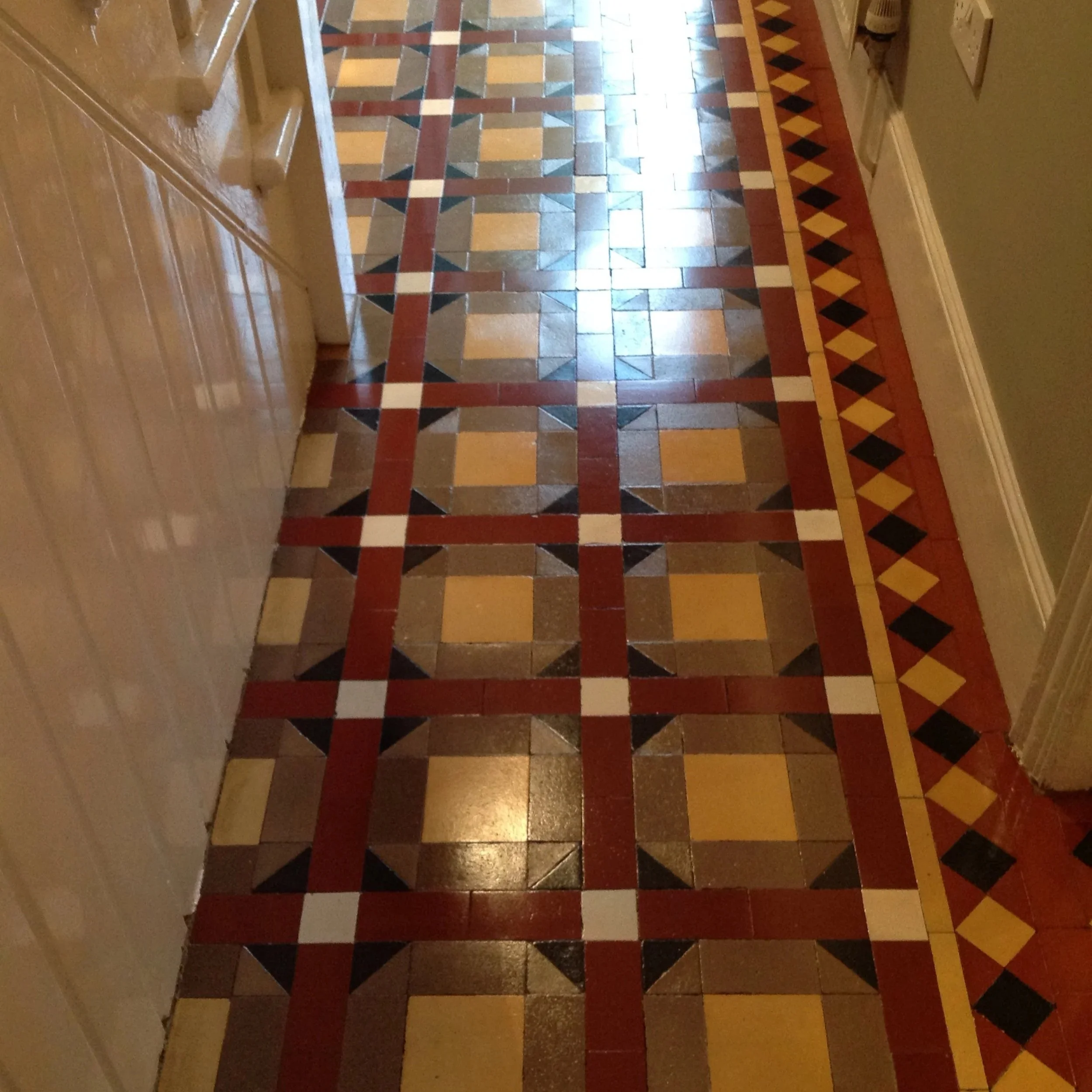 Decorative tile floor with geometric pattern in red, black, yellow, and white in a hallway.