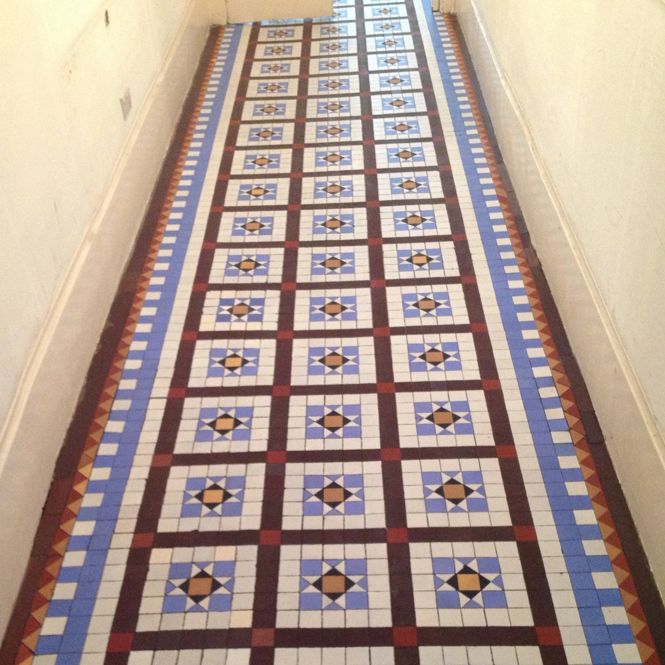 Long hallway with a colorful tiled floor featuring geometric patterns in shades of white, blue, black, red, and tan.