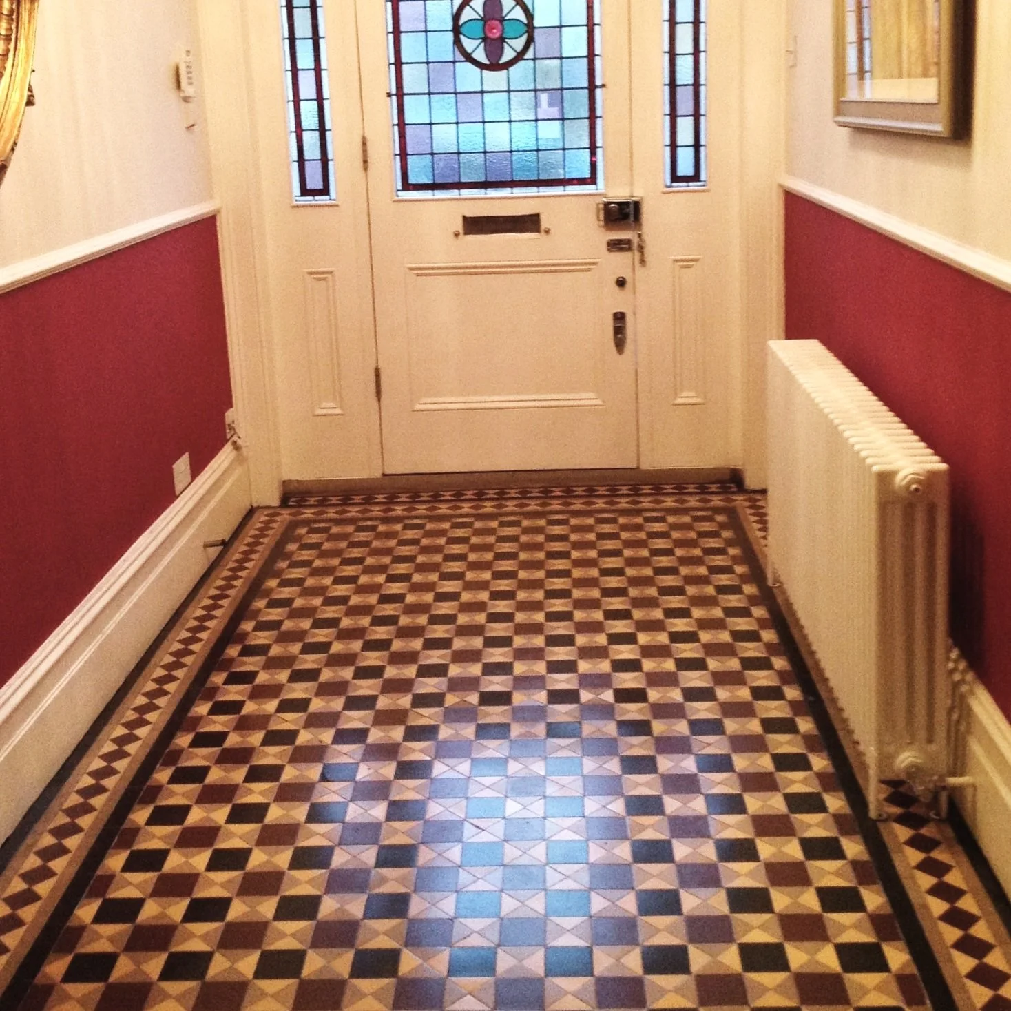 Entry hallway with patterned tile floor, cream-colored door with stained glass window, red and cream walls, and a white radiator on the right.