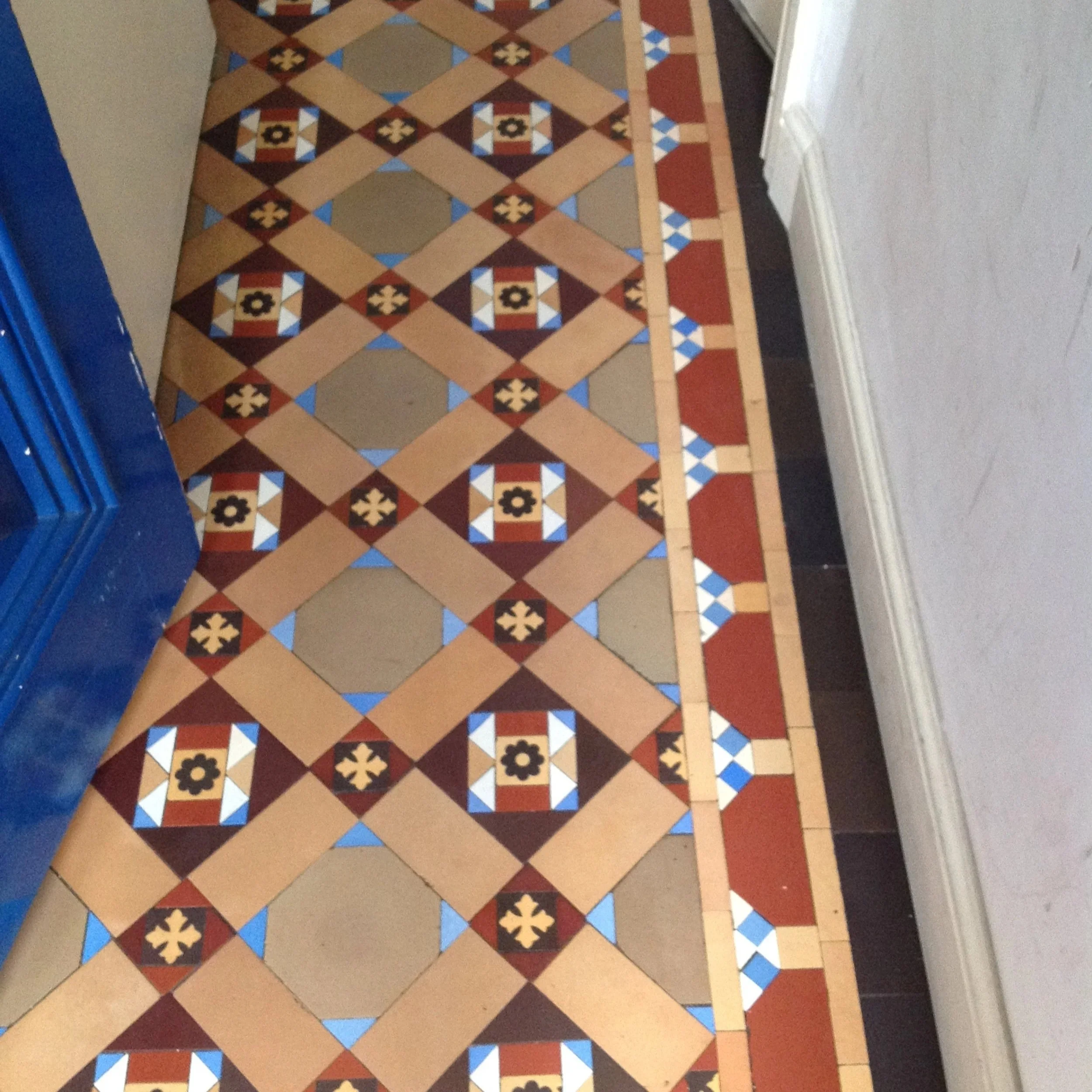 Patterned tile floor with geometric and floral designs in shades of beige, brown, red, blue, and white.