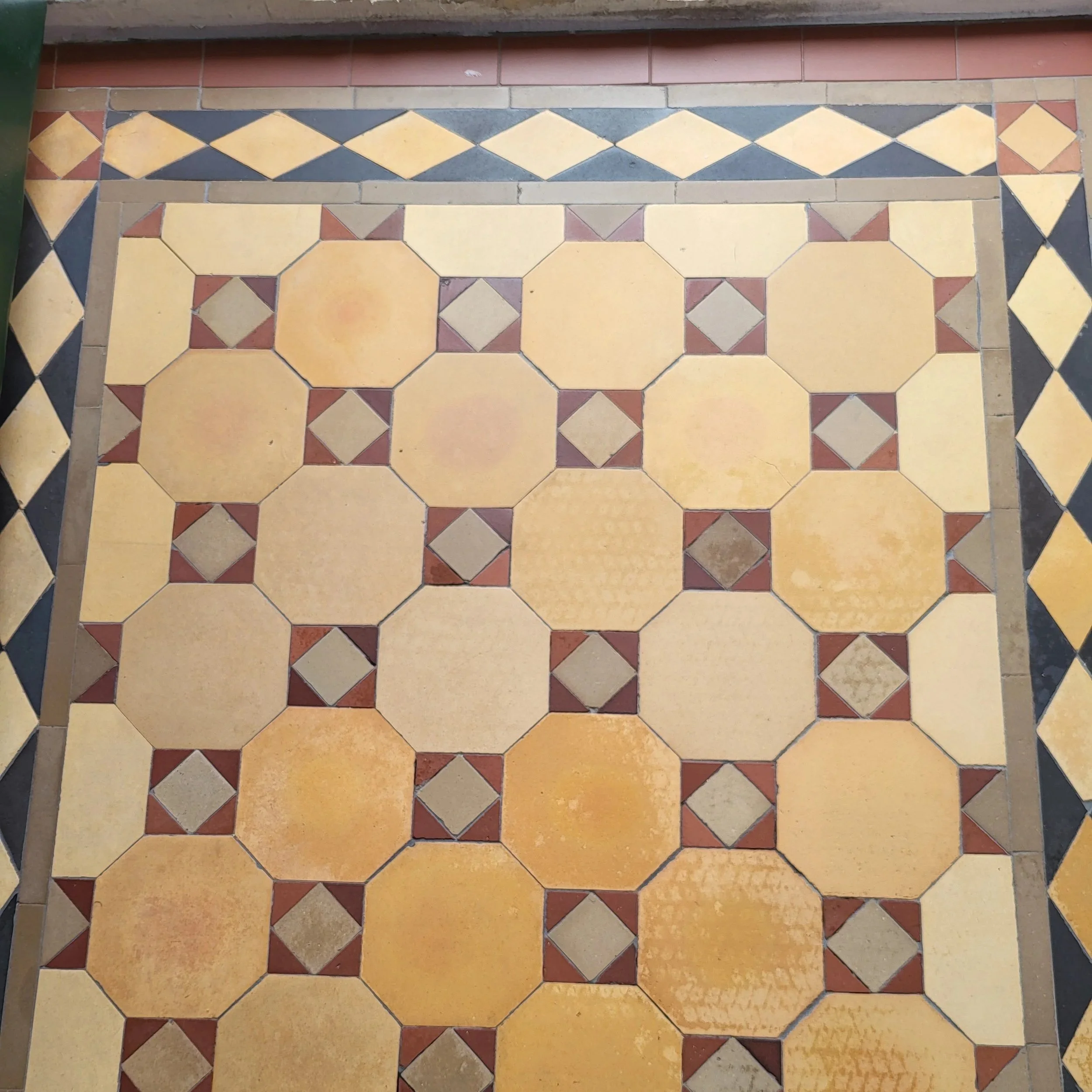 Patterned ceramic tile floor with large beige and orange octagon tiles, small red and beige diamond and triangular accents, and a surrounding border of alternating beige and black diamonds.