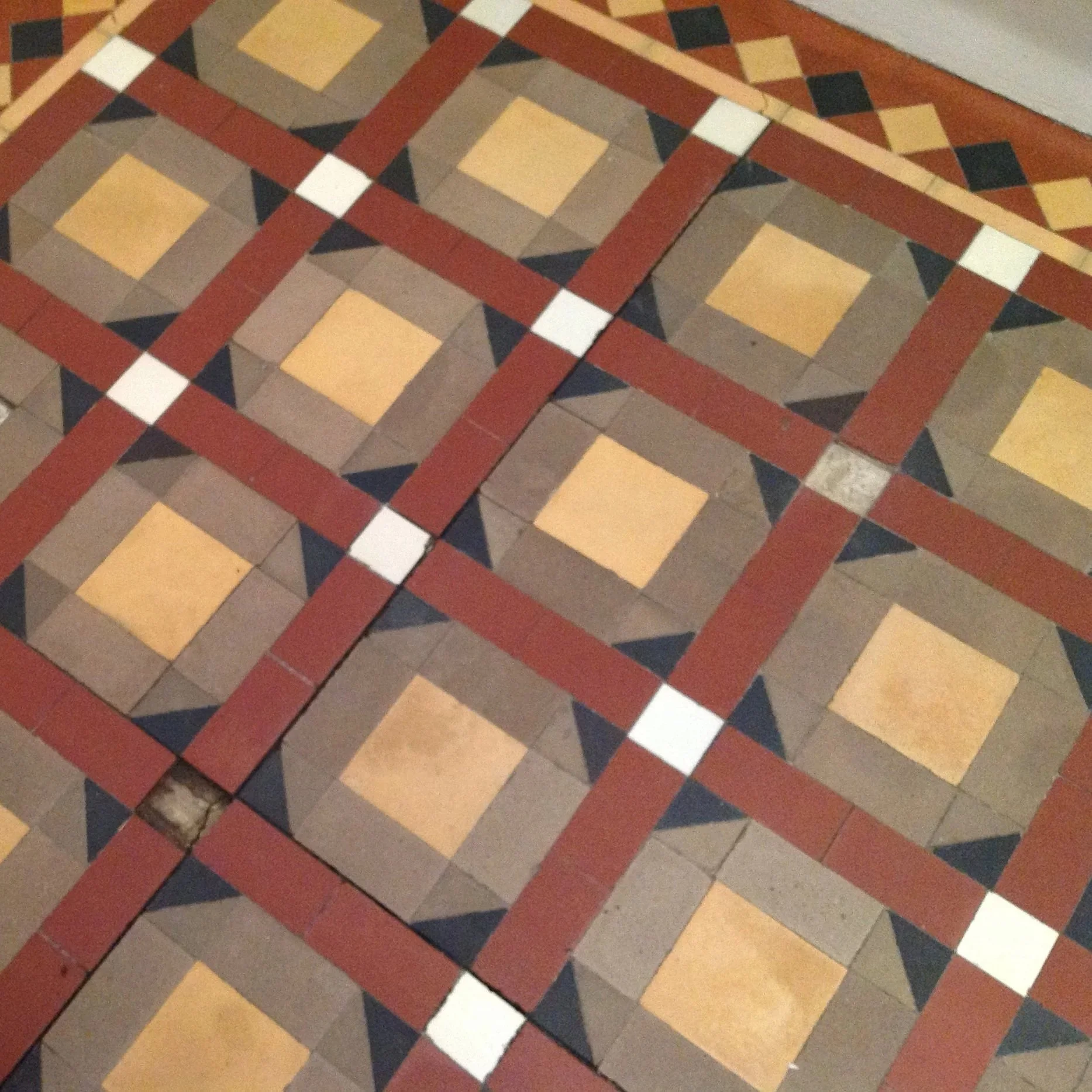 Patterned tile floor with geometric design in brown, red, black, and beige colors.