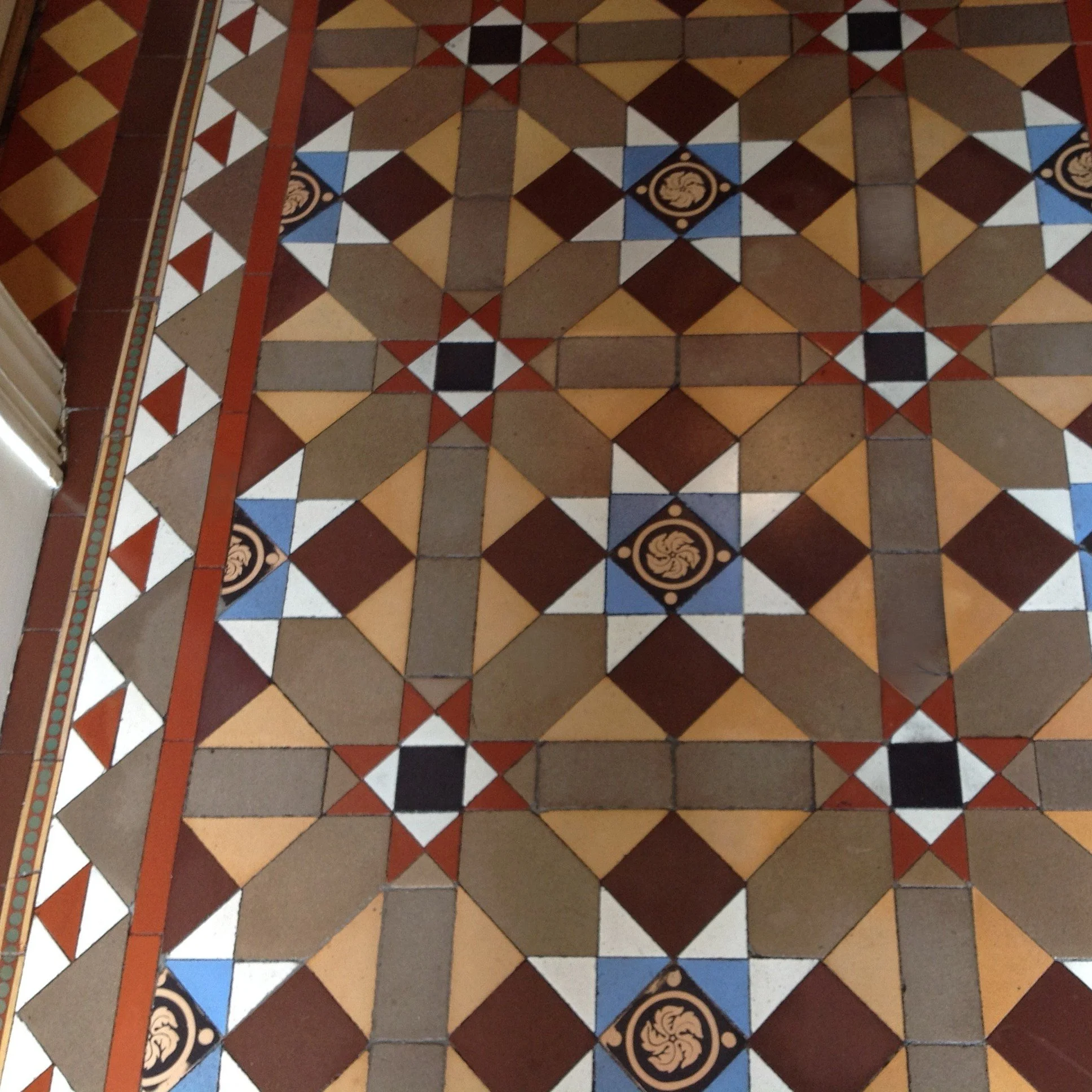 Decorative geometric tile floor with intricate patterns in beige, black, white, blue, and reddish-brown colors.
