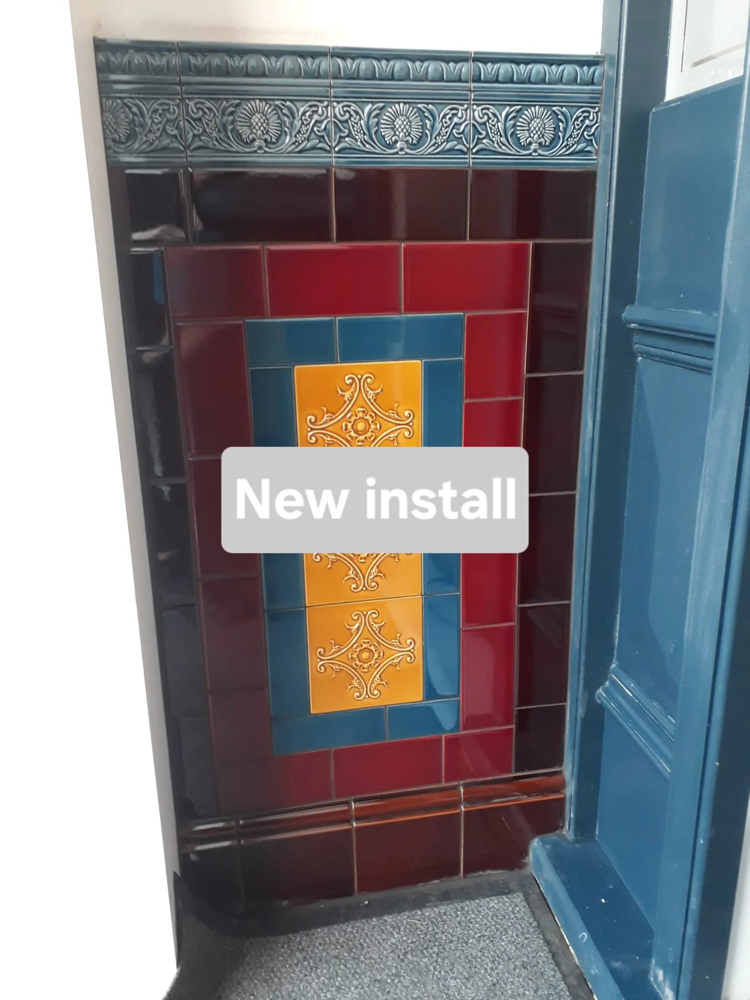 Close-up of a colorful decorative tile wall with the words 'New install' overlaid. The tiles are arranged in a pattern with a mix of dark red, blue, yellow, and ornamental designs.
