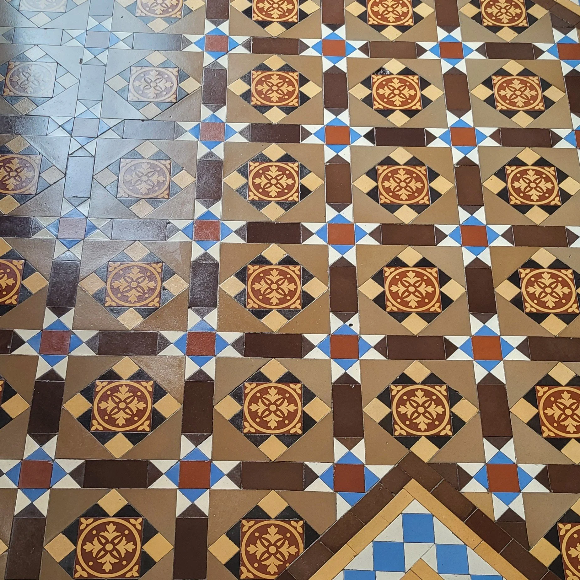 Patterned tile floor with geometric and floral designs in colors brown, beige, black, blue, and red.