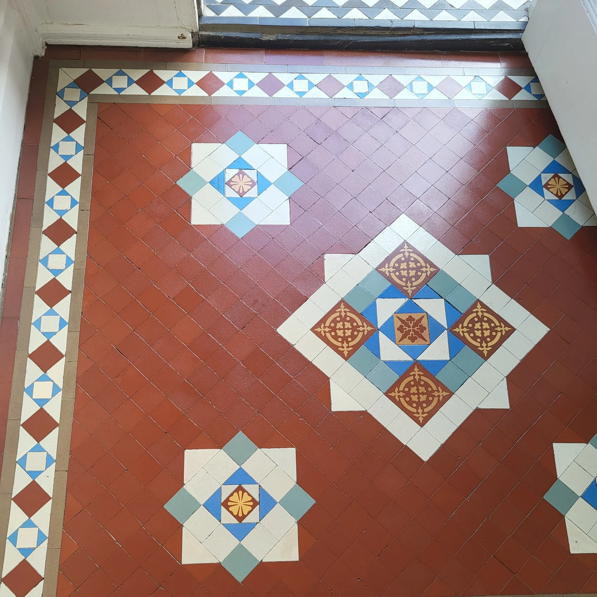 Picture of beautiful tiled hallway near the front door in red with a centralised white and encaustic motif surrounded by four simpler motifs. A typical Edwardian format