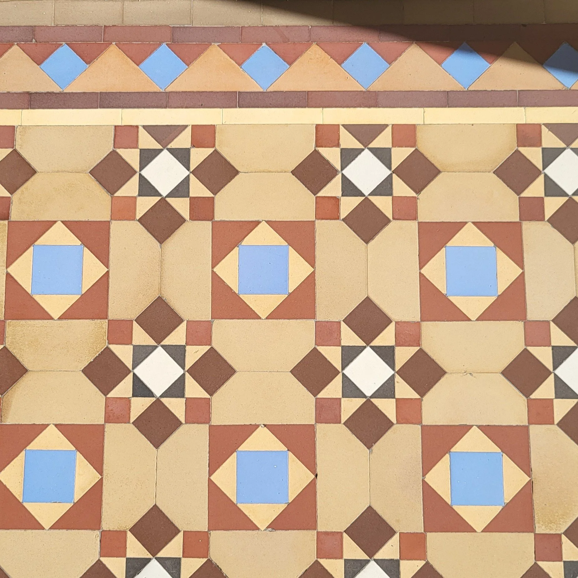 Photo of tiled floor taken from above in mainly coffee half six inch octagon tiles with bright blue and orange accents